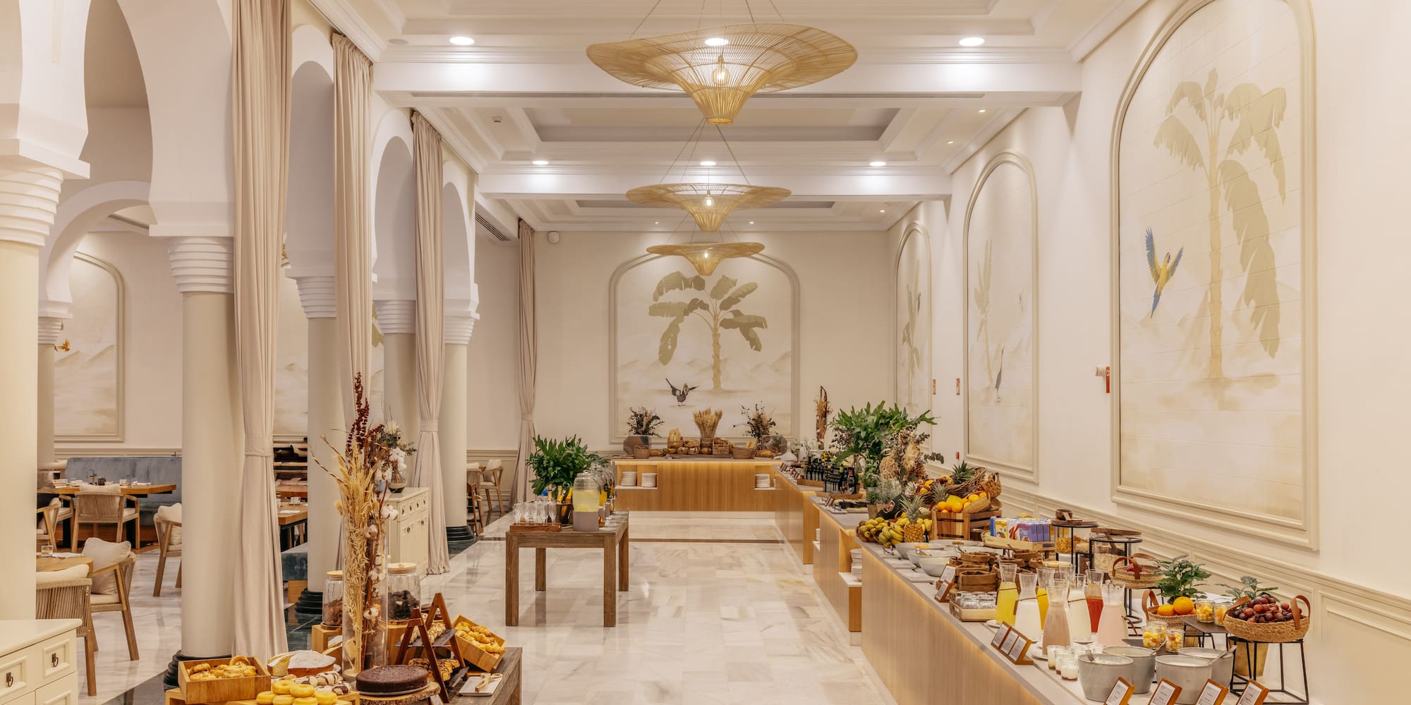 Tropical hotel buffet breakfast with palm murals, fresh fruit, and pastries.