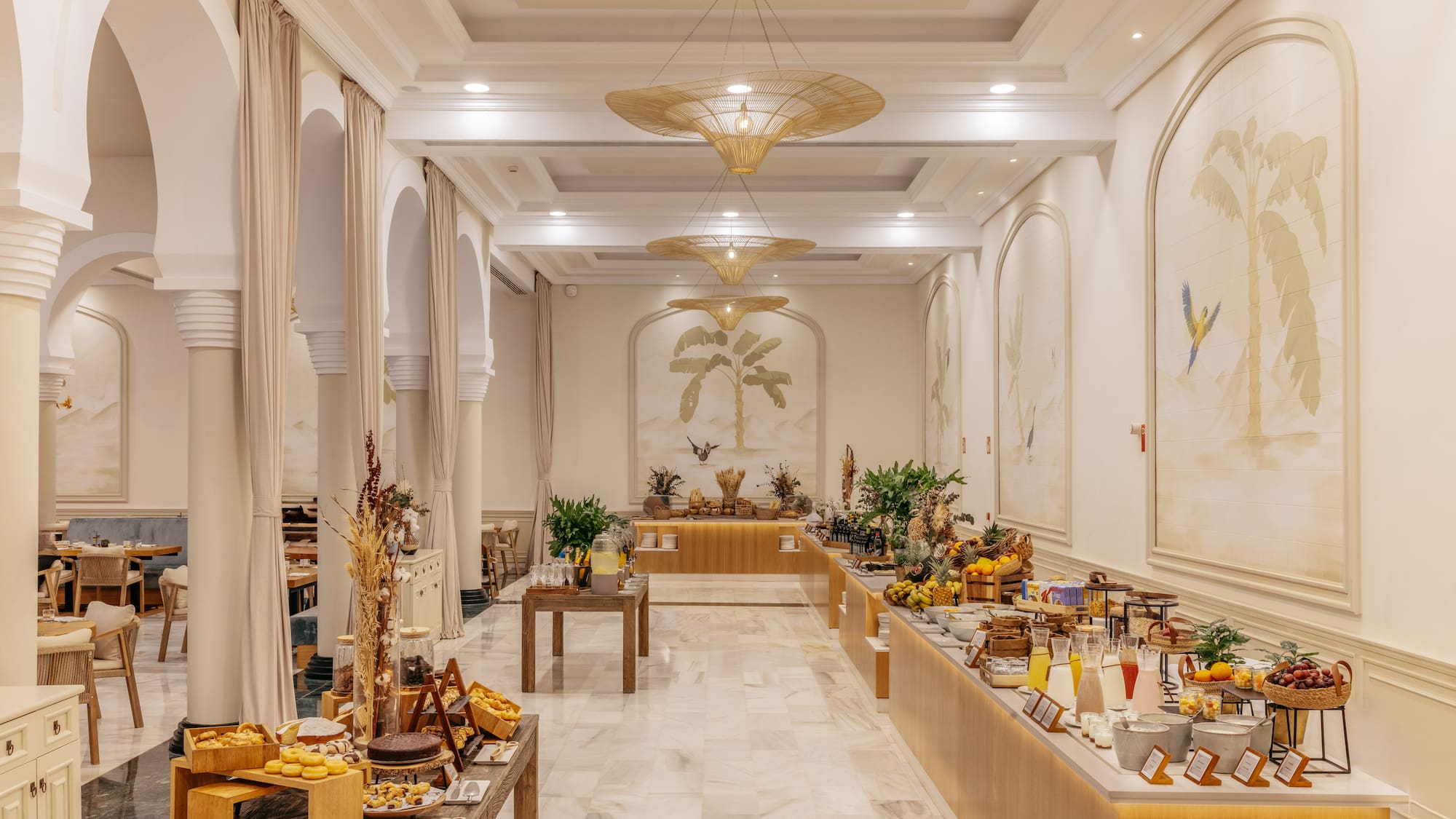 Tropical hotel buffet breakfast with palm murals, fresh fruit, and pastries.