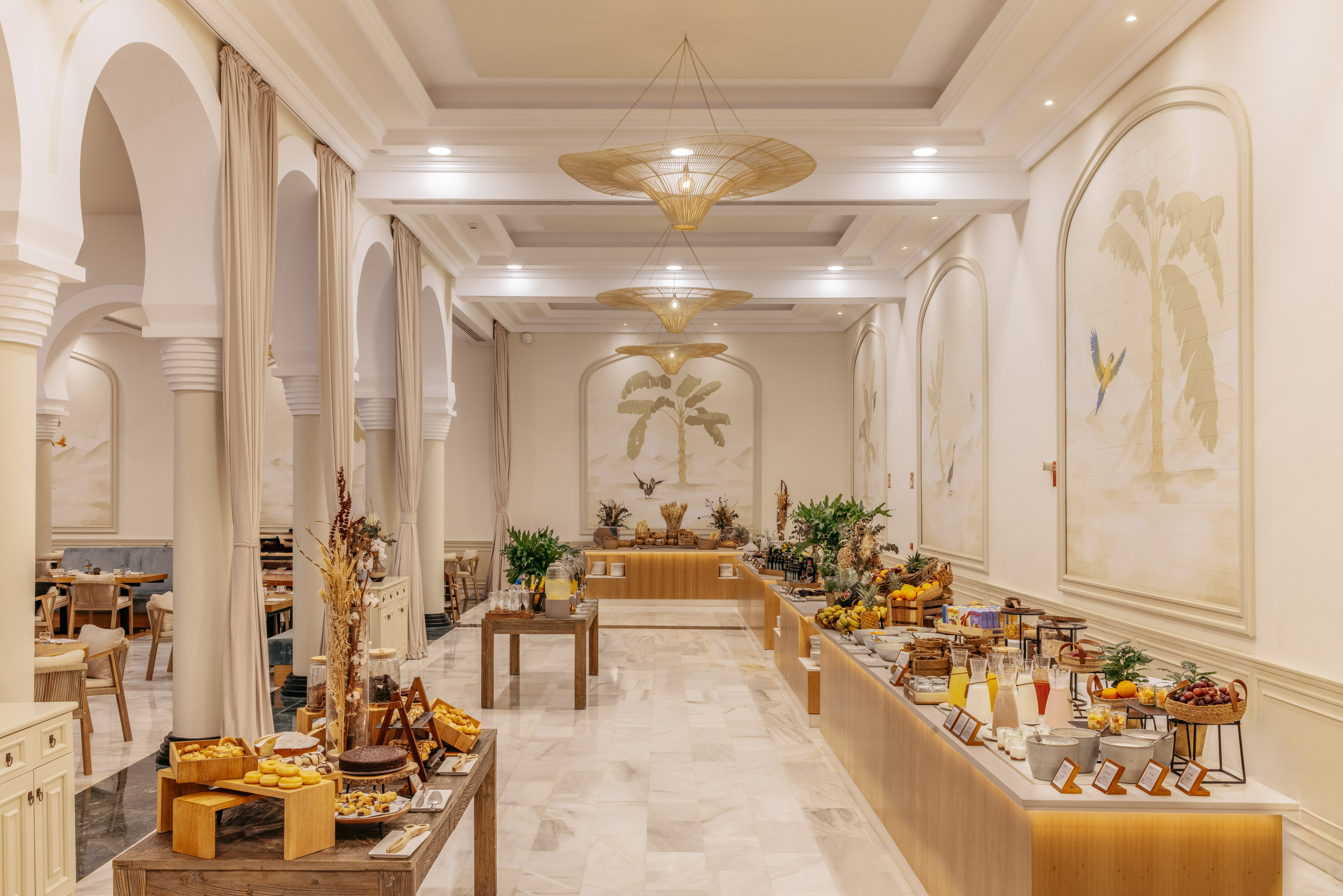 Tropical hotel buffet breakfast with palm murals, fresh fruit, and pastries.