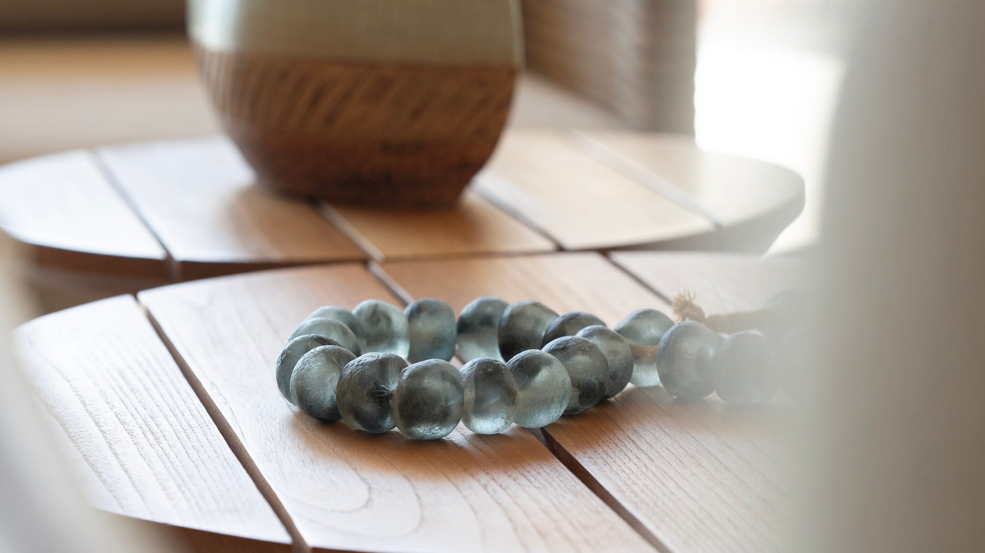 Blue-green glass bead bracelet, woven vase on wooden side tables, home decor.