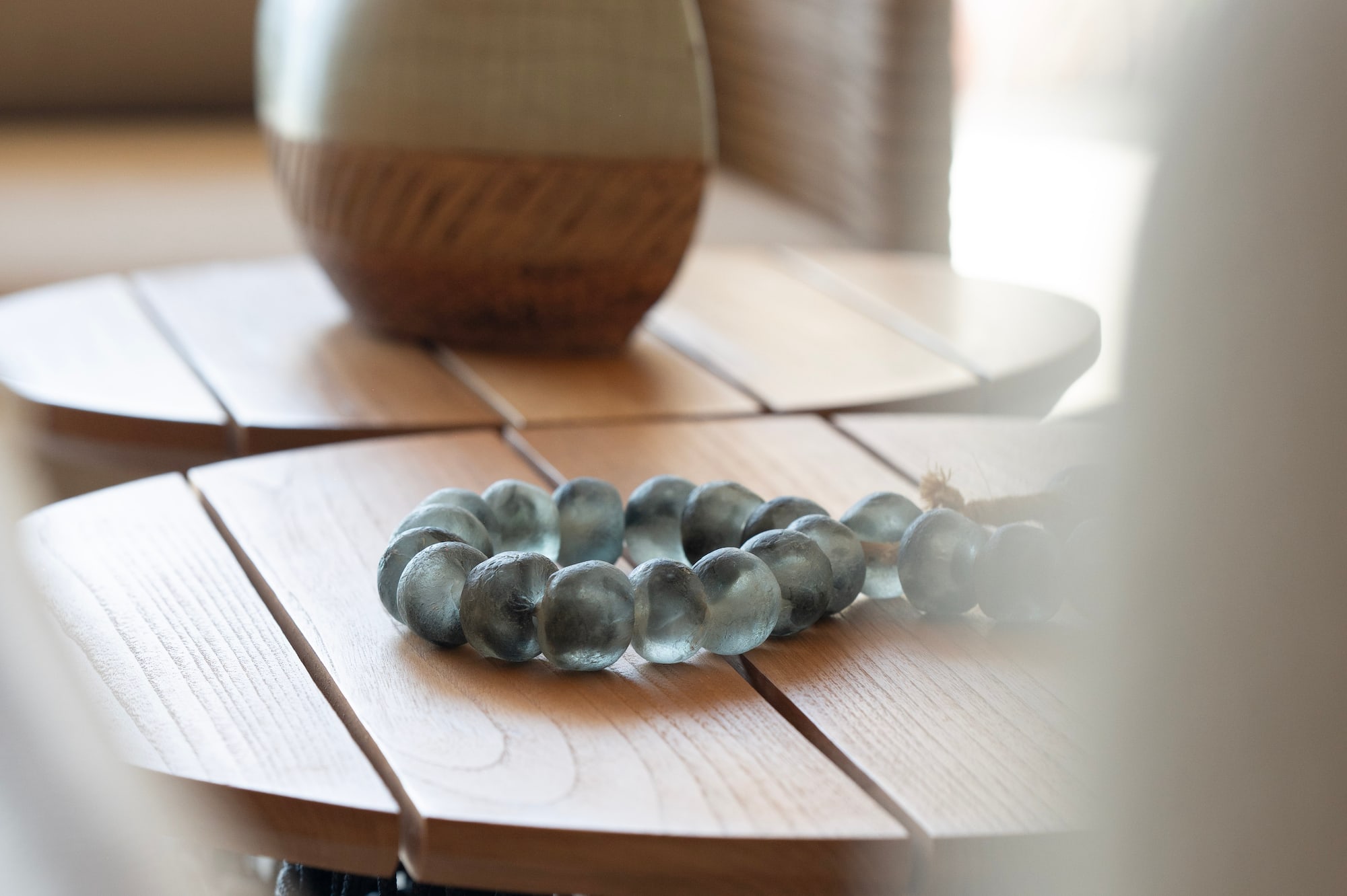 Blue-green glass bead bracelet, woven vase on wooden side tables, home decor.