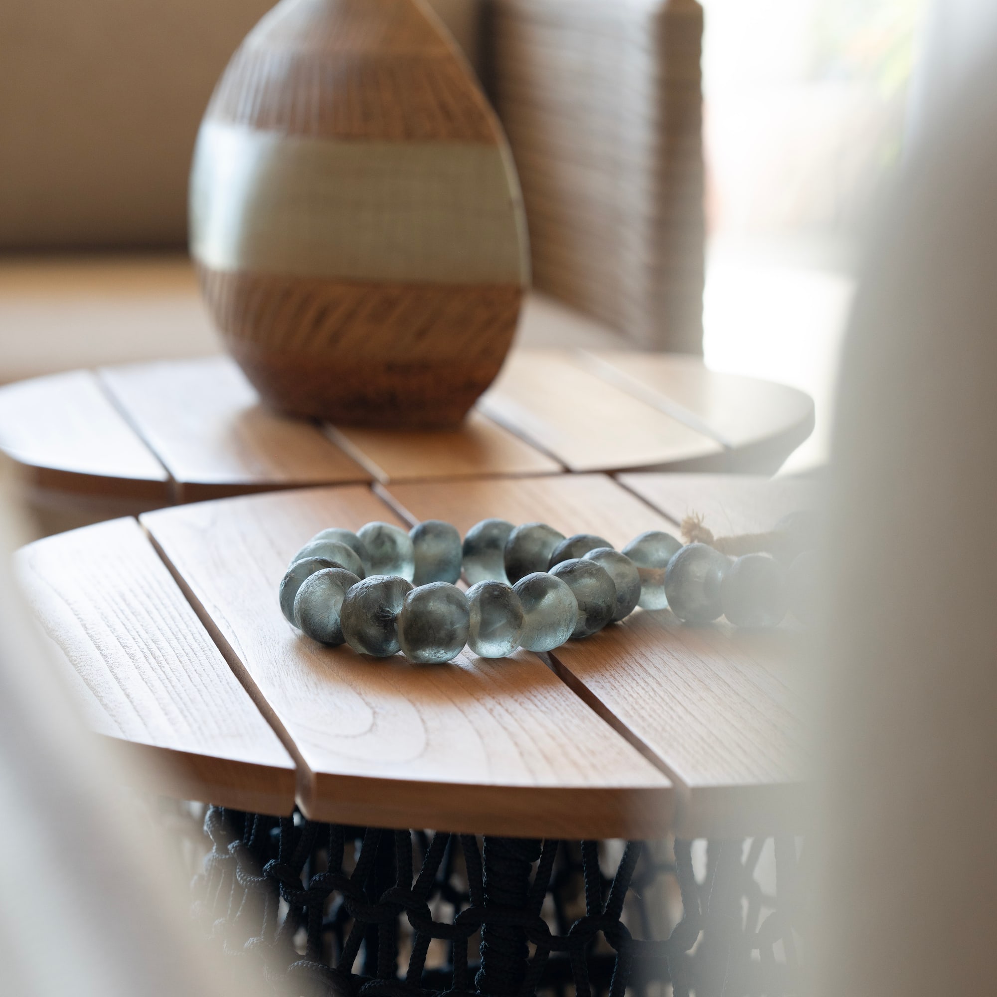 Blue-green glass bead bracelet, woven vase on wooden side tables, home decor.