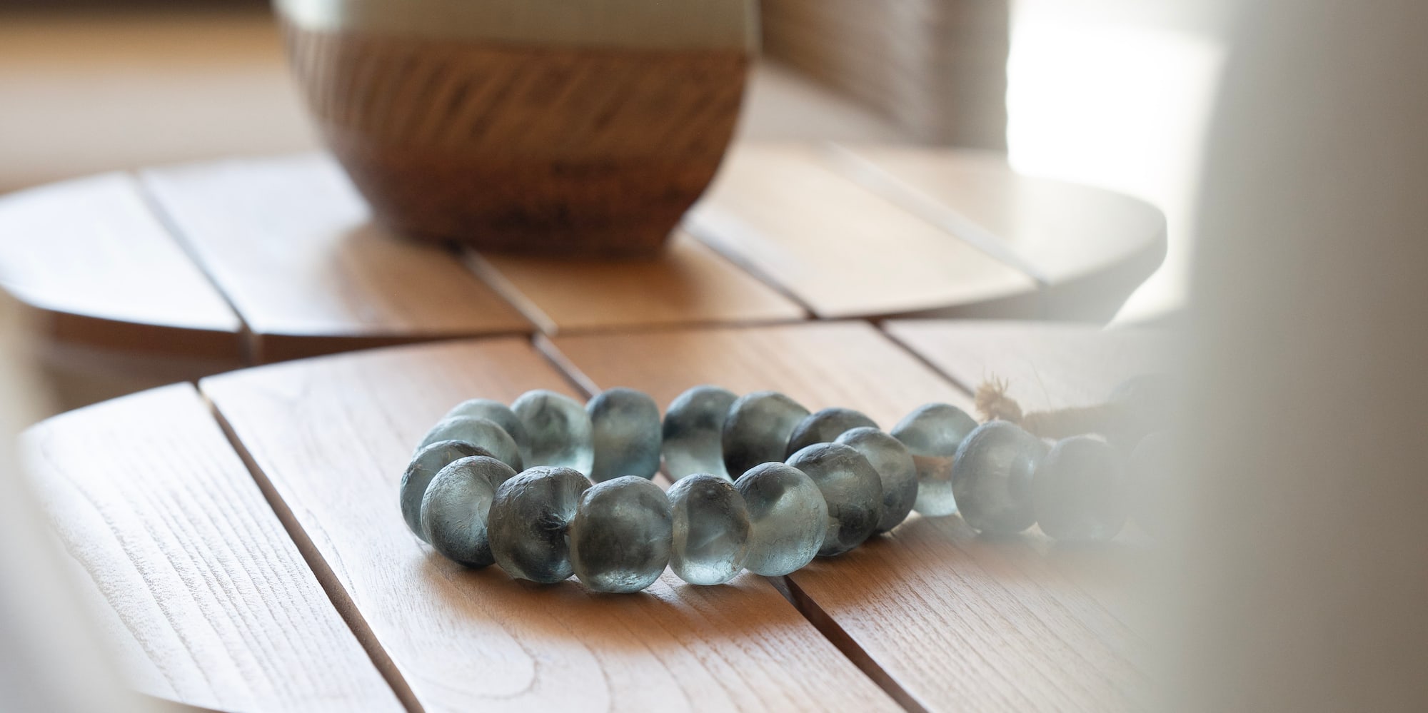 Blue-green glass bead bracelet, woven vase on wooden side tables, home decor.