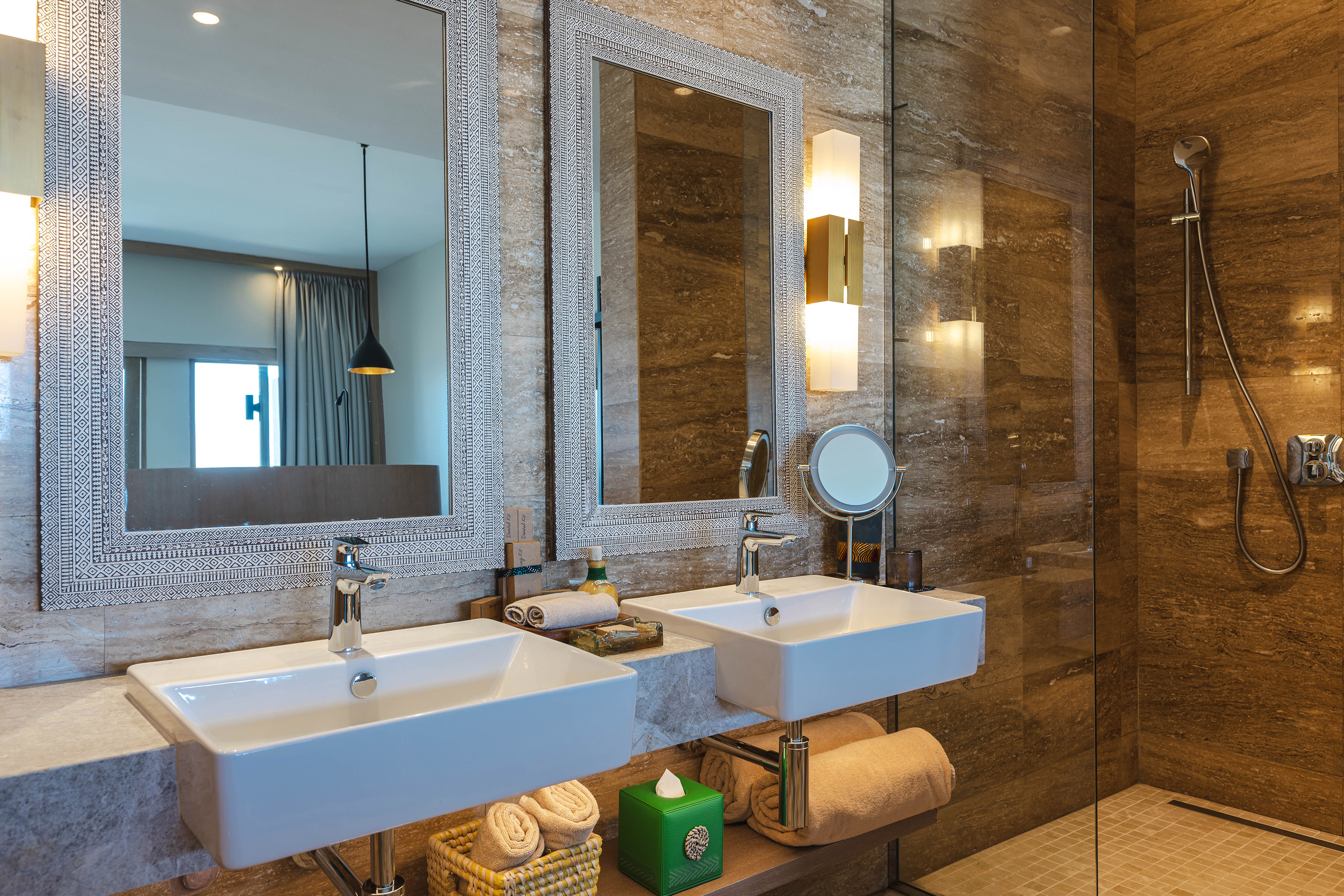 Modern bathroom with double vanity, patterned mirrors, marble walls, and glass shower.