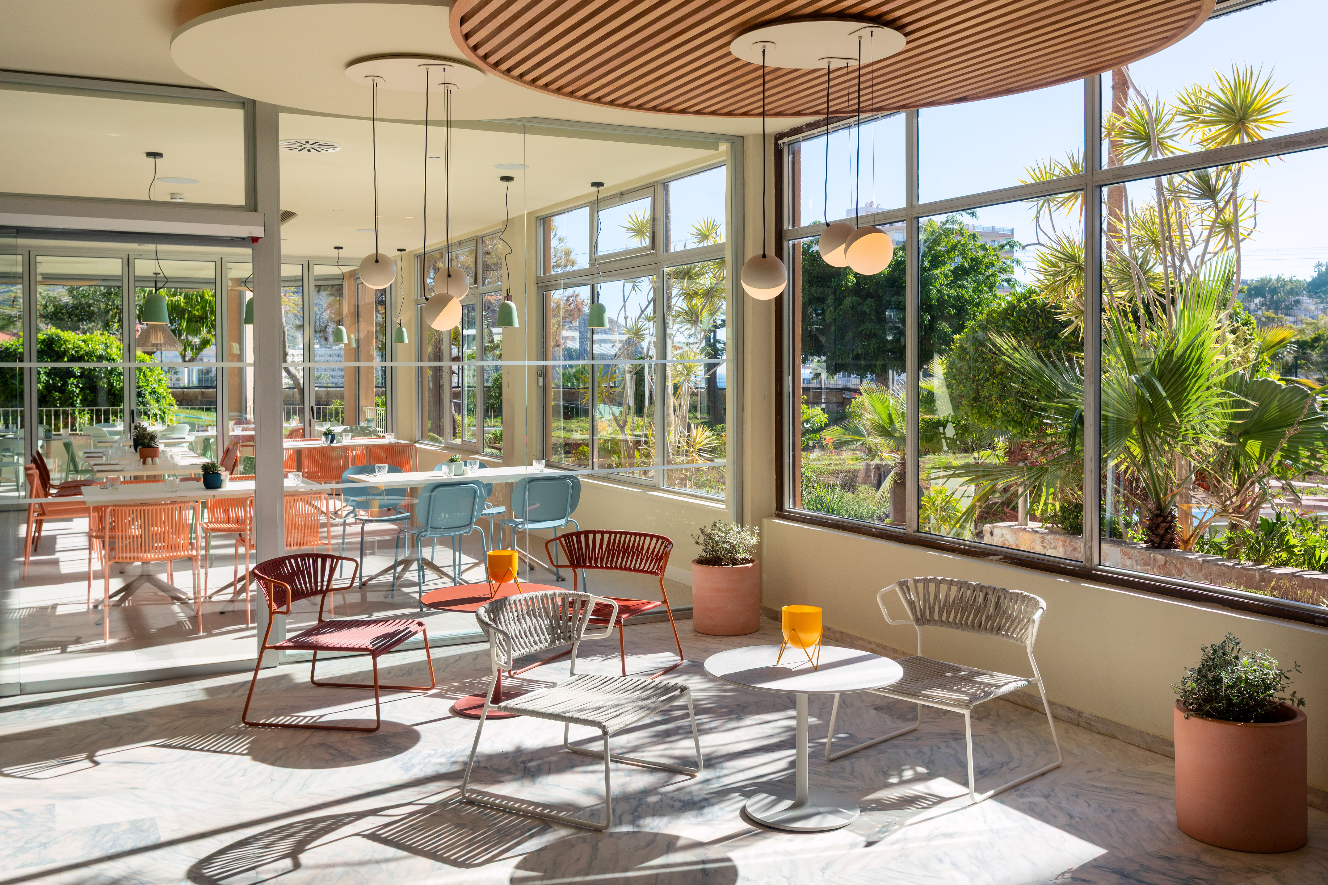 Contemporary cafe with colorful seating, large windows, and lush garden view.