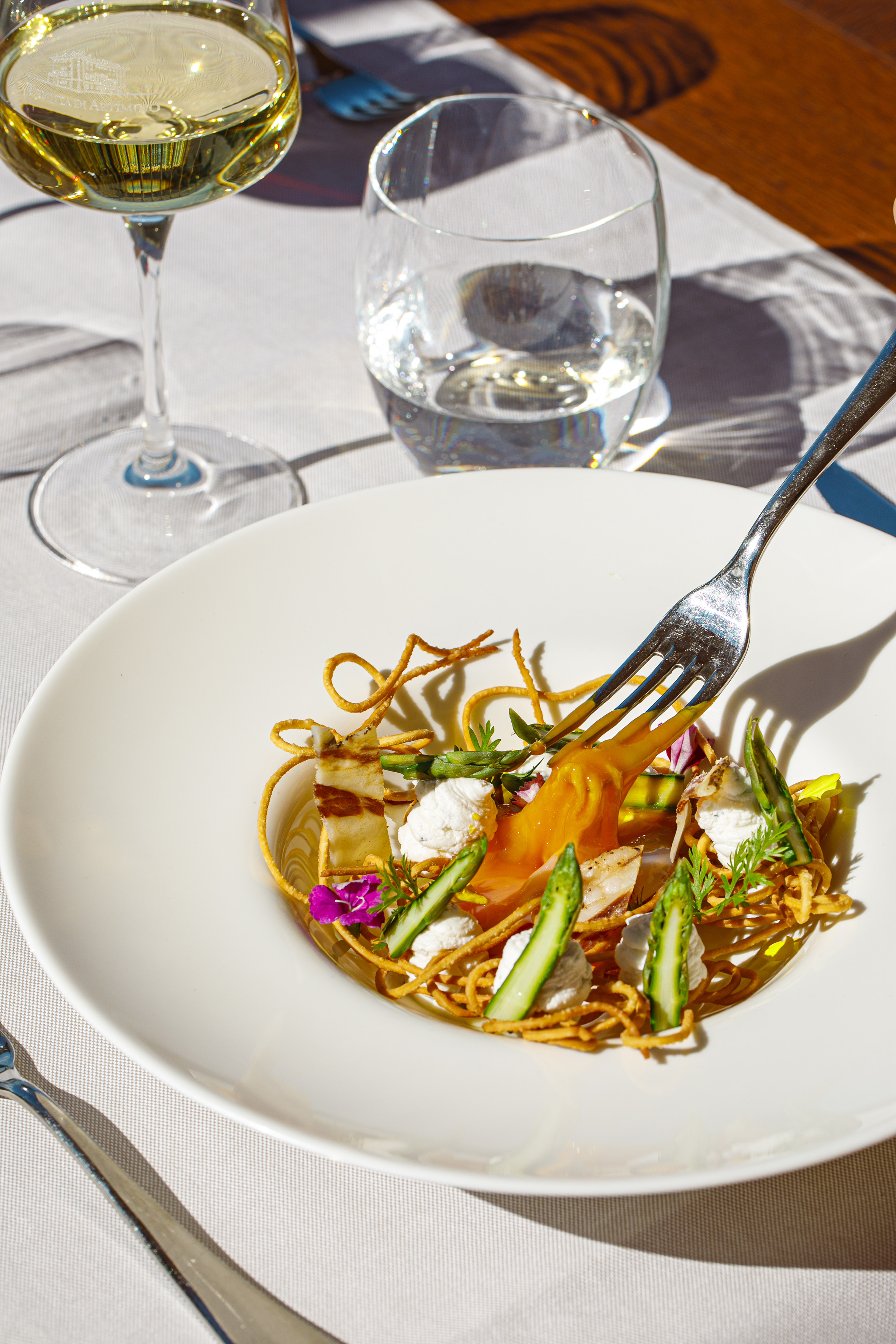 Elegant plate with asparagus, golden spirals, cream, fork, white wine, water.