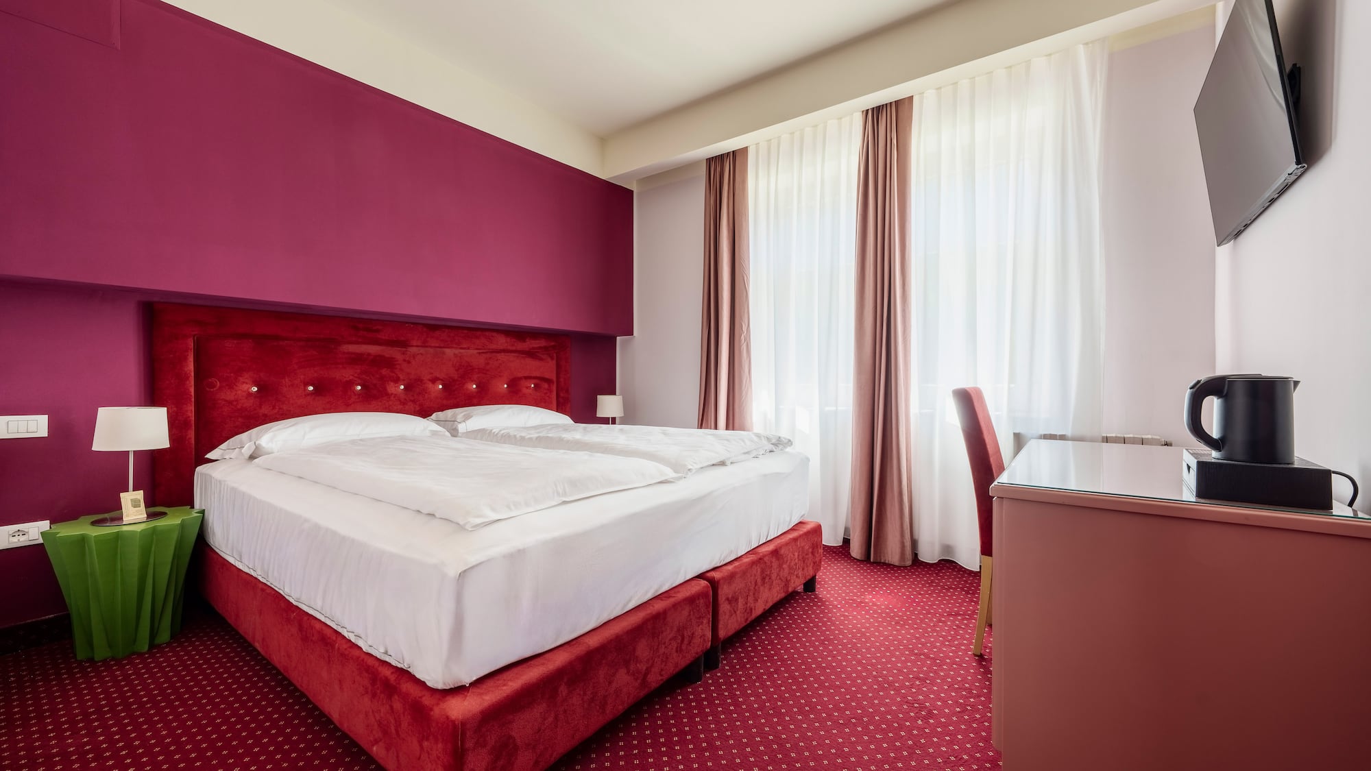 Modern hotel room with red bed, magenta wall, and patterned red carpet.