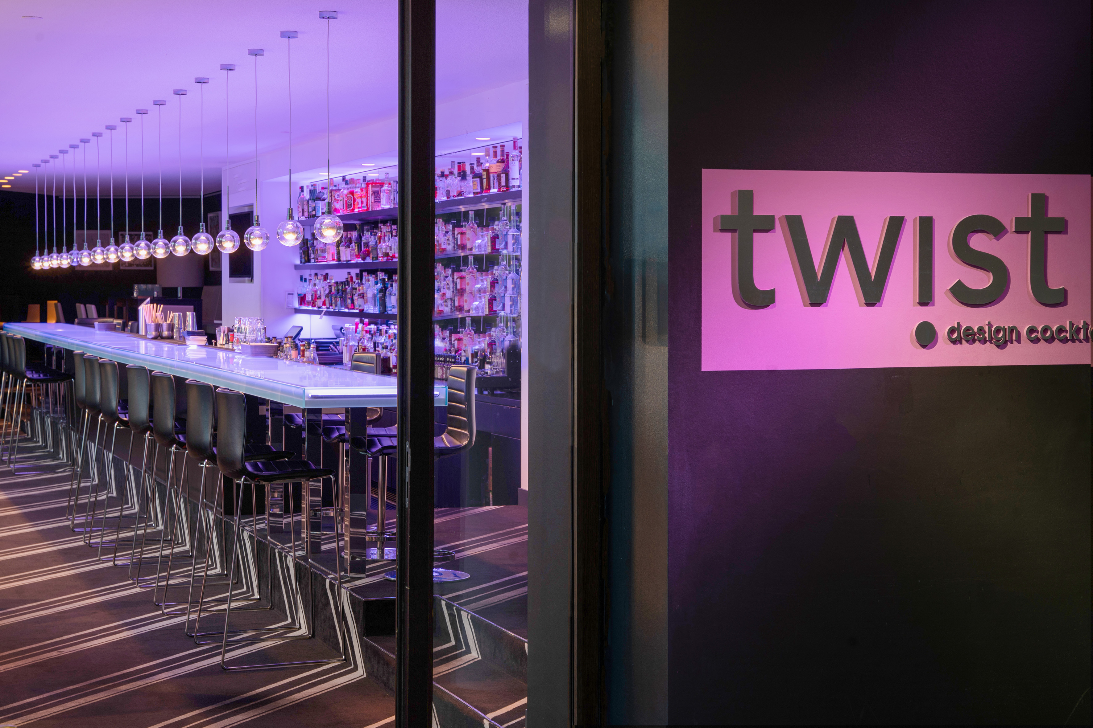 Twist cocktail bar with purple lighting, long bar, liquor bottles, and stools. - Twist Bar, Apéritifs - INNSiDE Dresden, Dresde