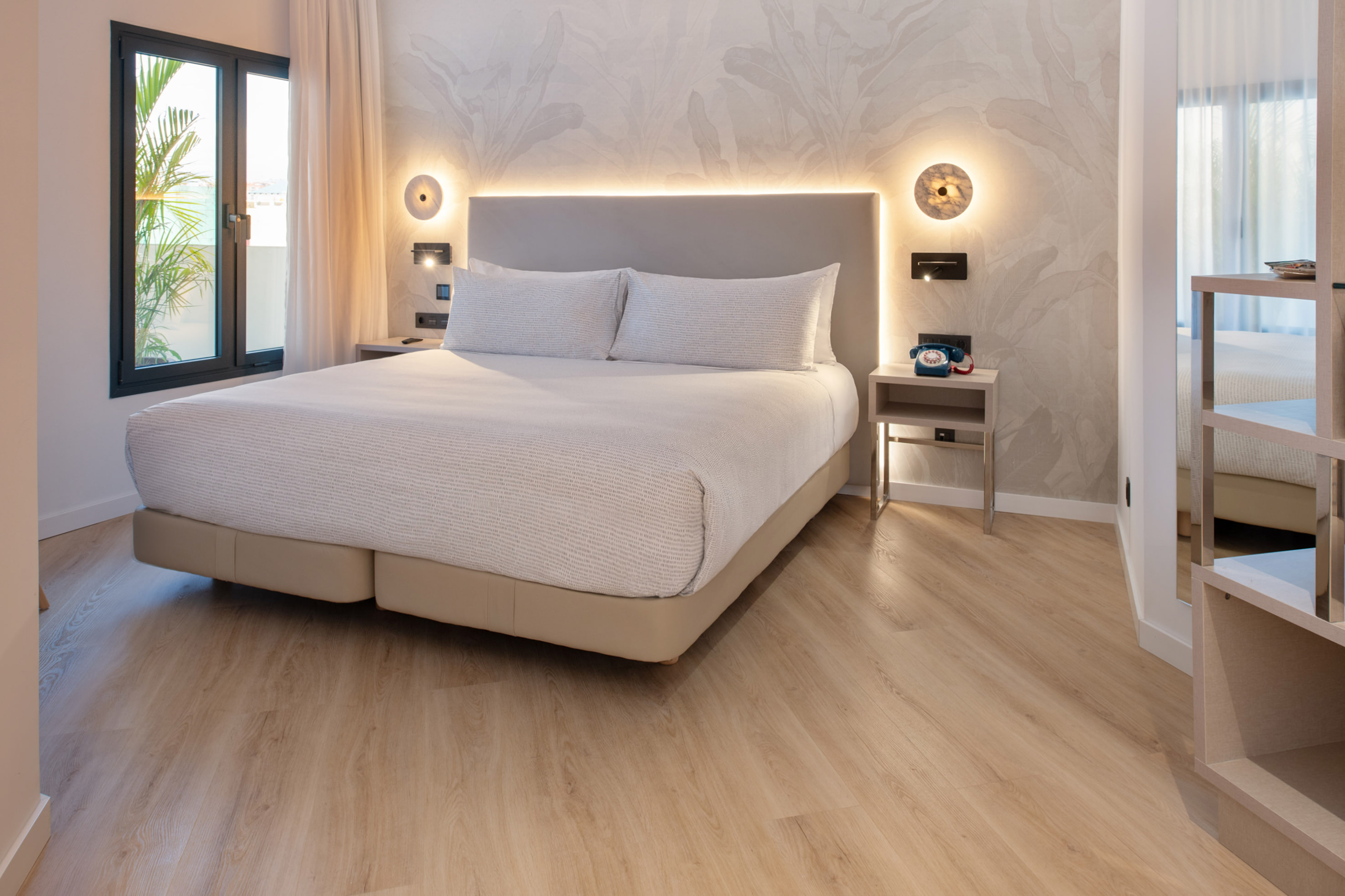 Modern hotel bedroom with king bed, light wood floor, and scenic window view.