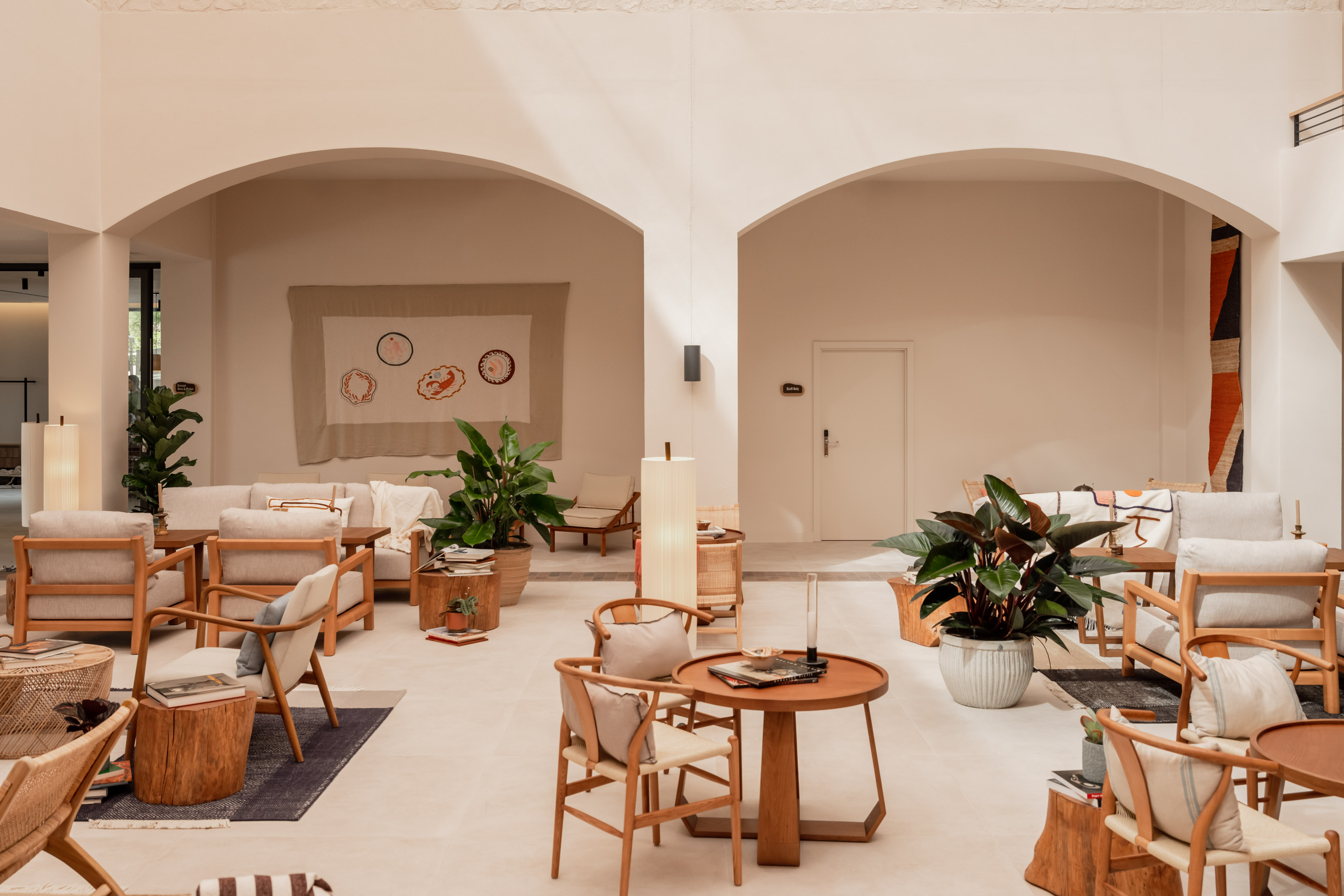 Modern hotel lounge with wood furniture, potted plants, and arched interiors.