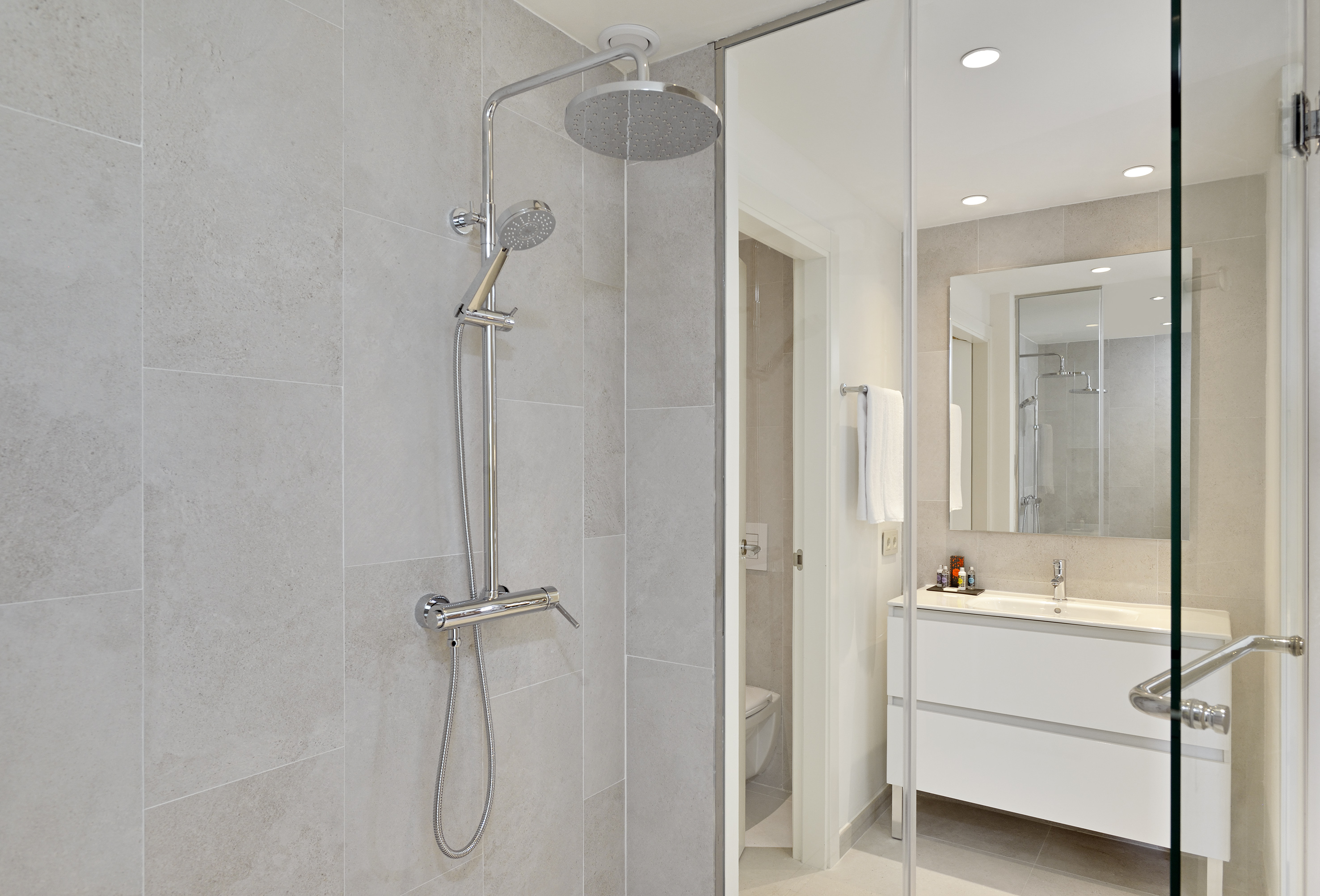 Modern bathroom with gray tiled shower, glass screen, rain shower, and vanity.