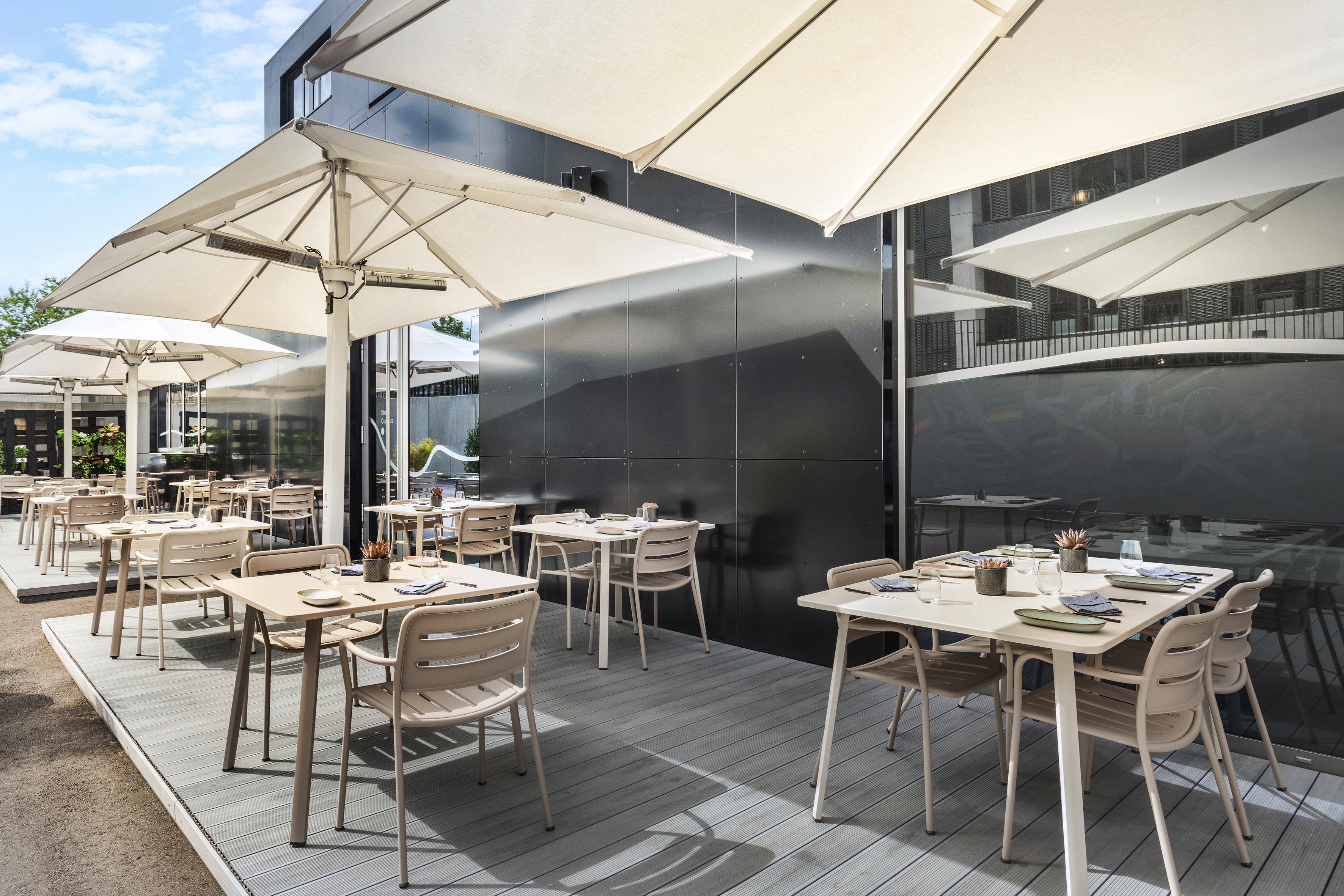Al fresco restaurant terrace with modern tables, chairs, and large white umbrellas. - INNSiDE Luxembourg, Luxemburgo