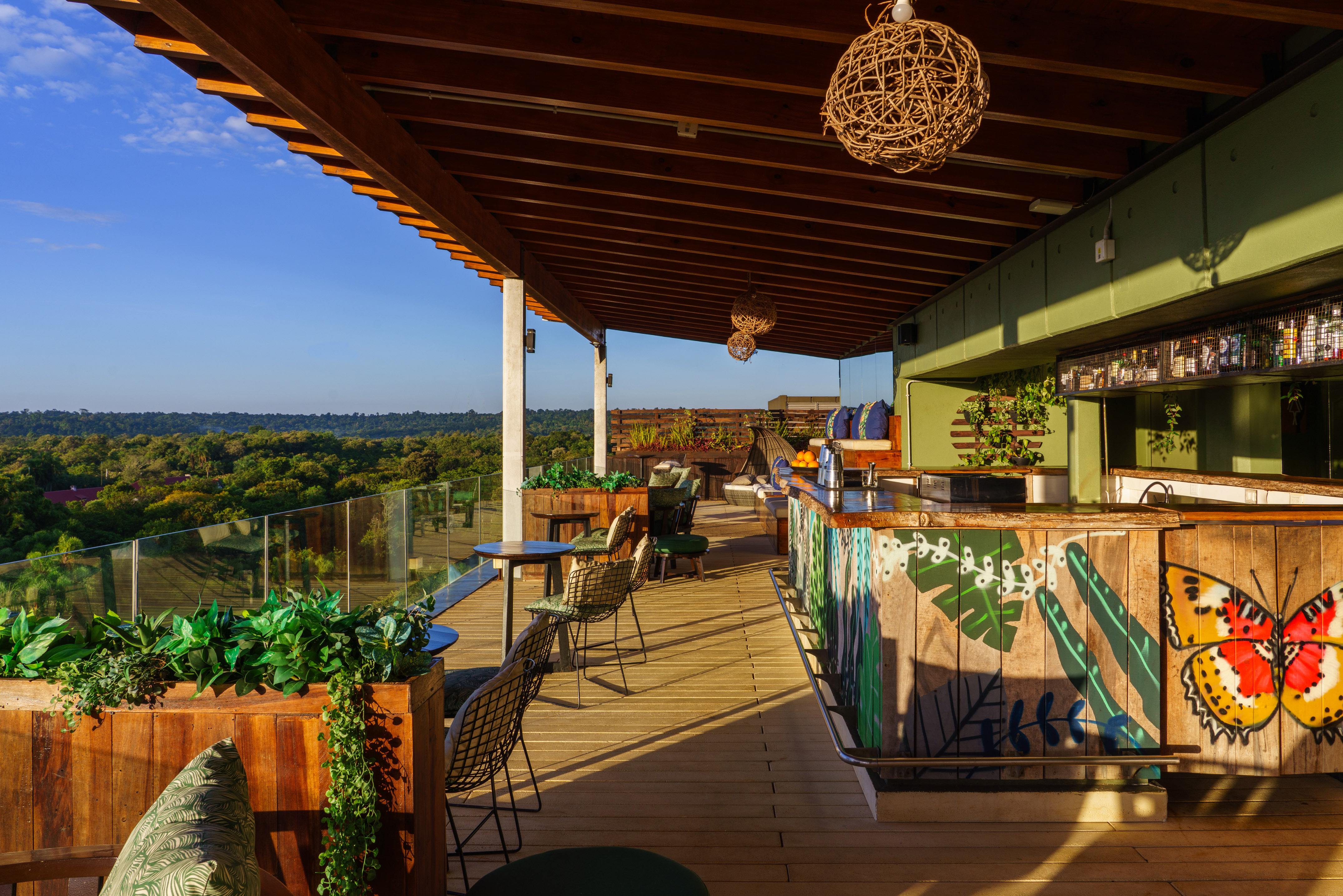 Rooftop bar with panoramic jungle view, wooden deck, and colorful bar art.