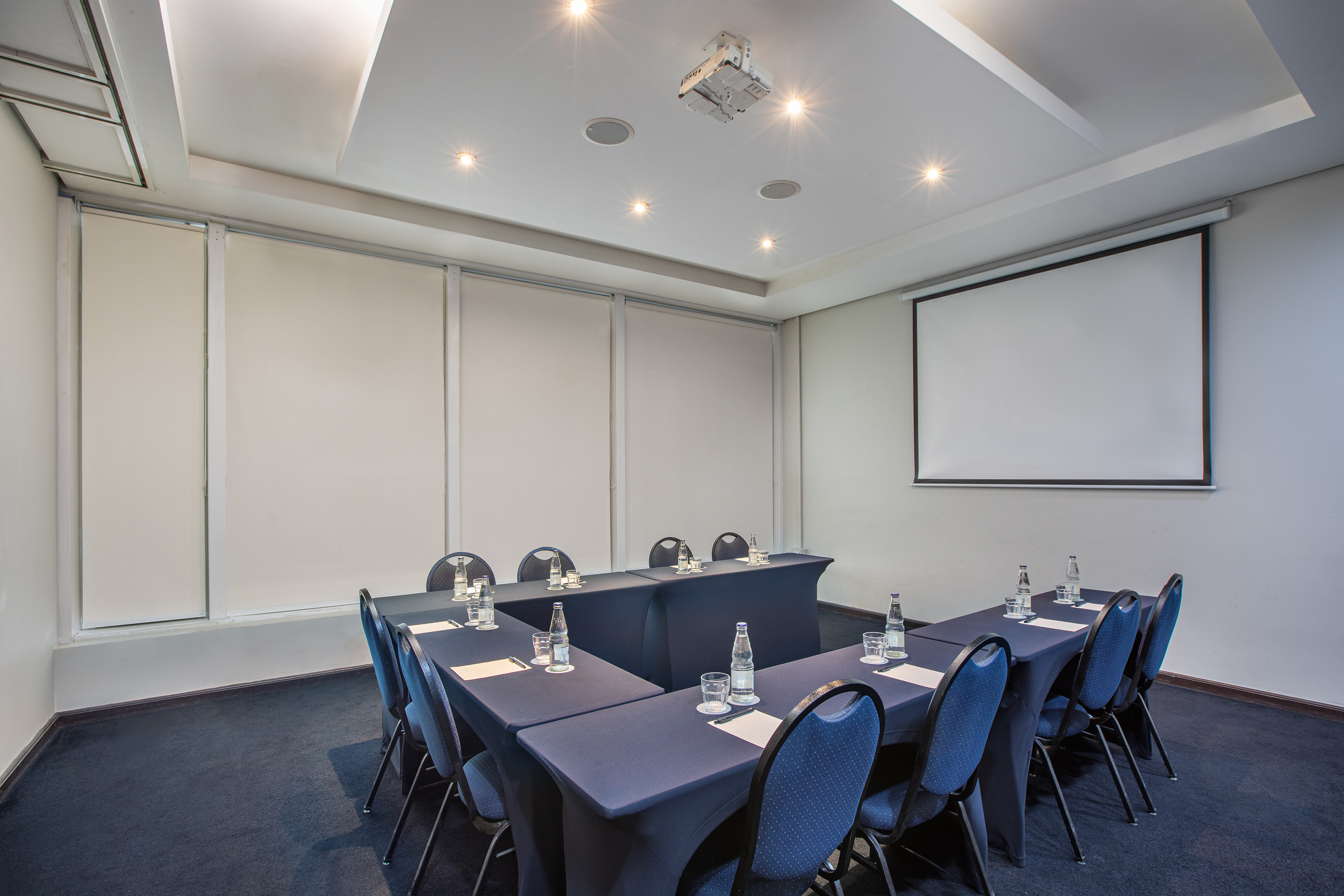 Conference room with U-shaped table, blue chairs, projector, and screen.