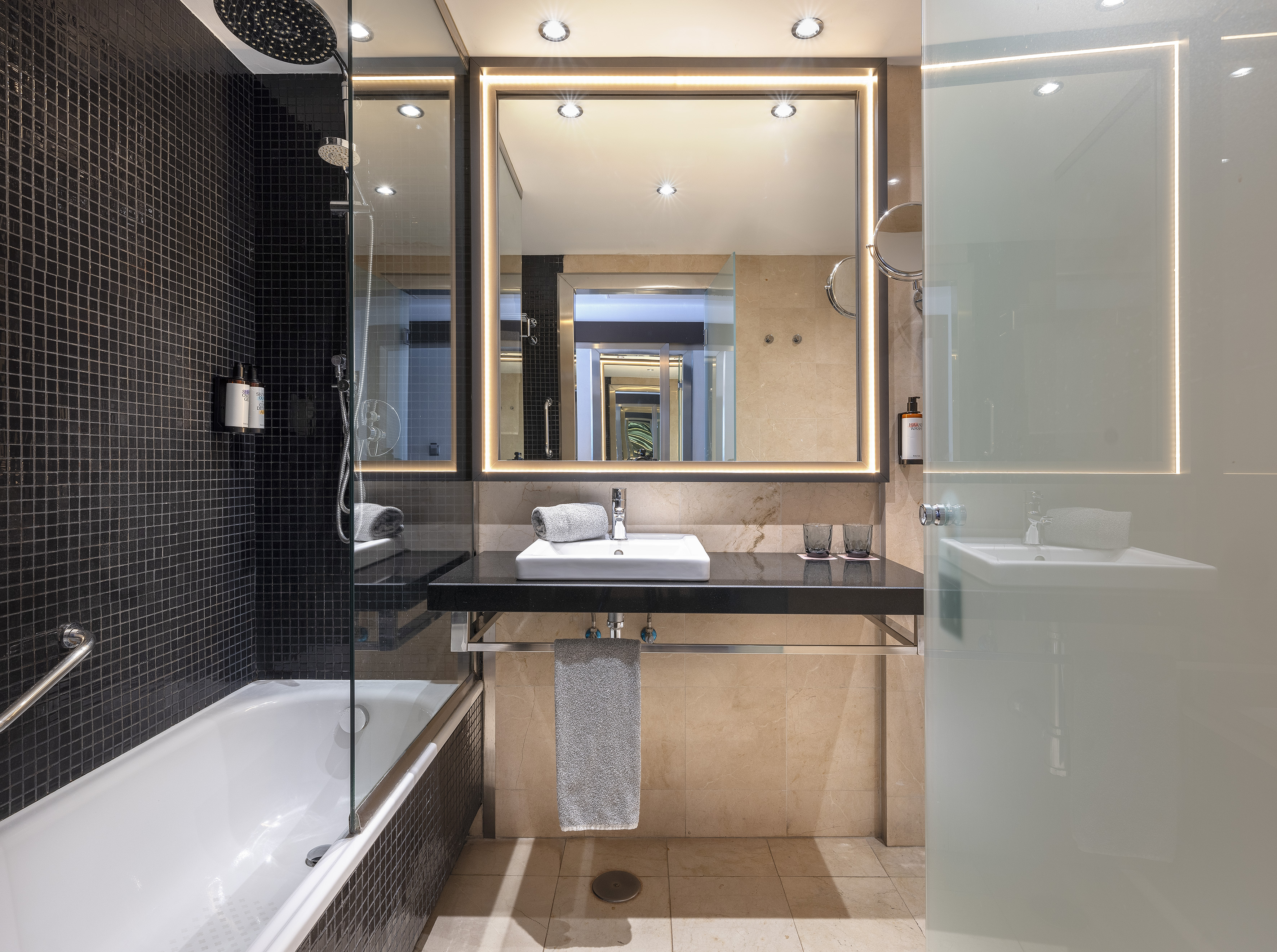 Modern bathroom with black tiled shower/tub, lit mirror, and vanity.