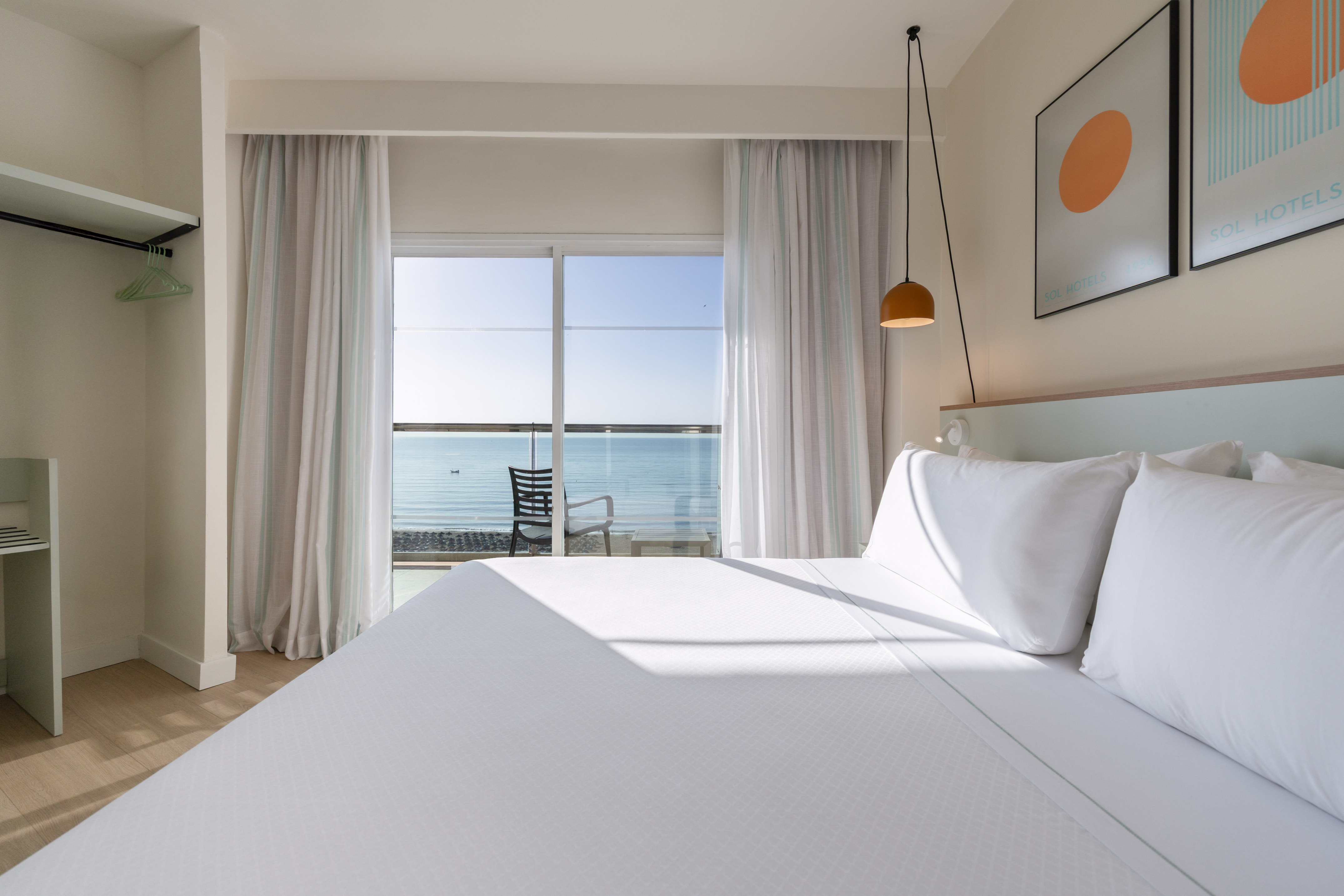 Ocean view hotel room with bright white bed, balcony, and minimalist decor.