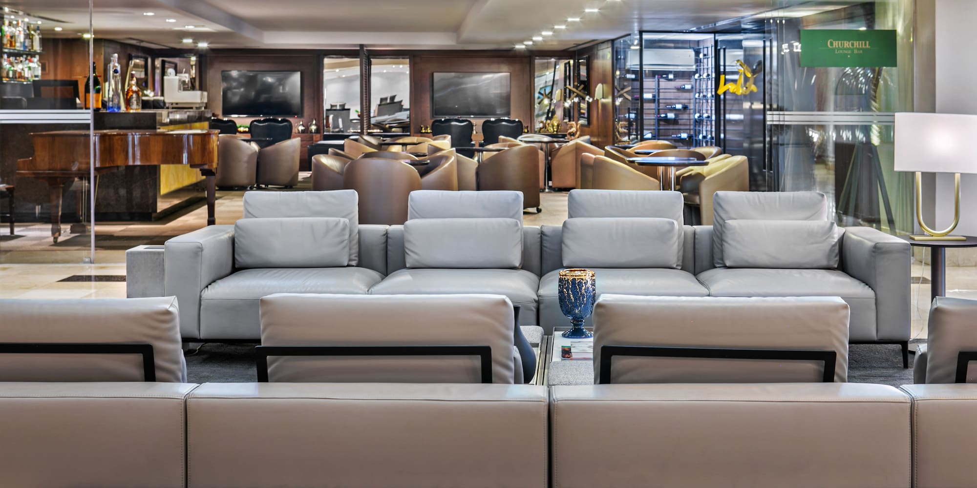 Churchill Lounge Bar interior with grey sofas, grand piano, and wine cellar.