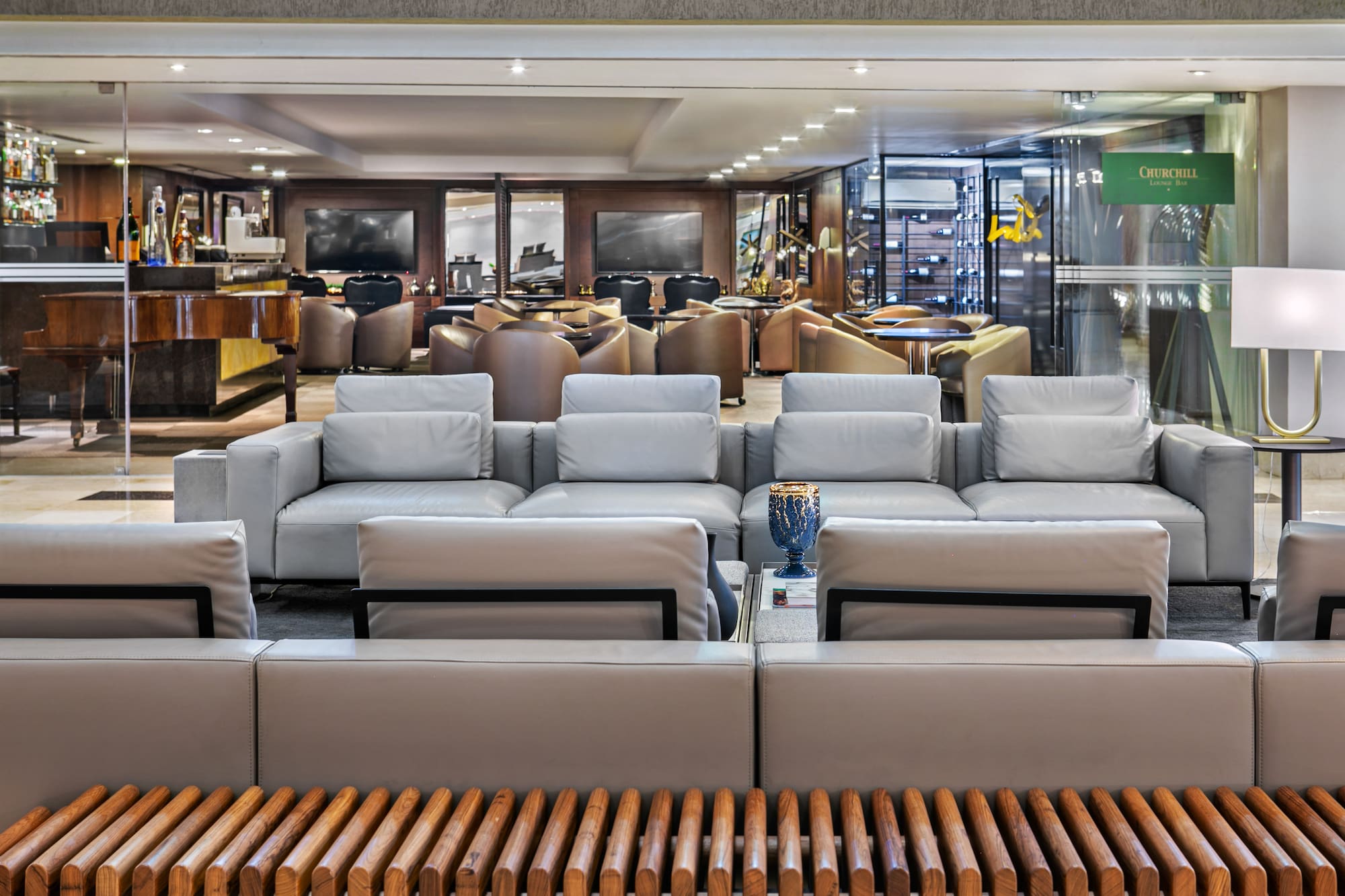 Churchill Lounge Bar interior with grey sofas, grand piano, and wine cellar.