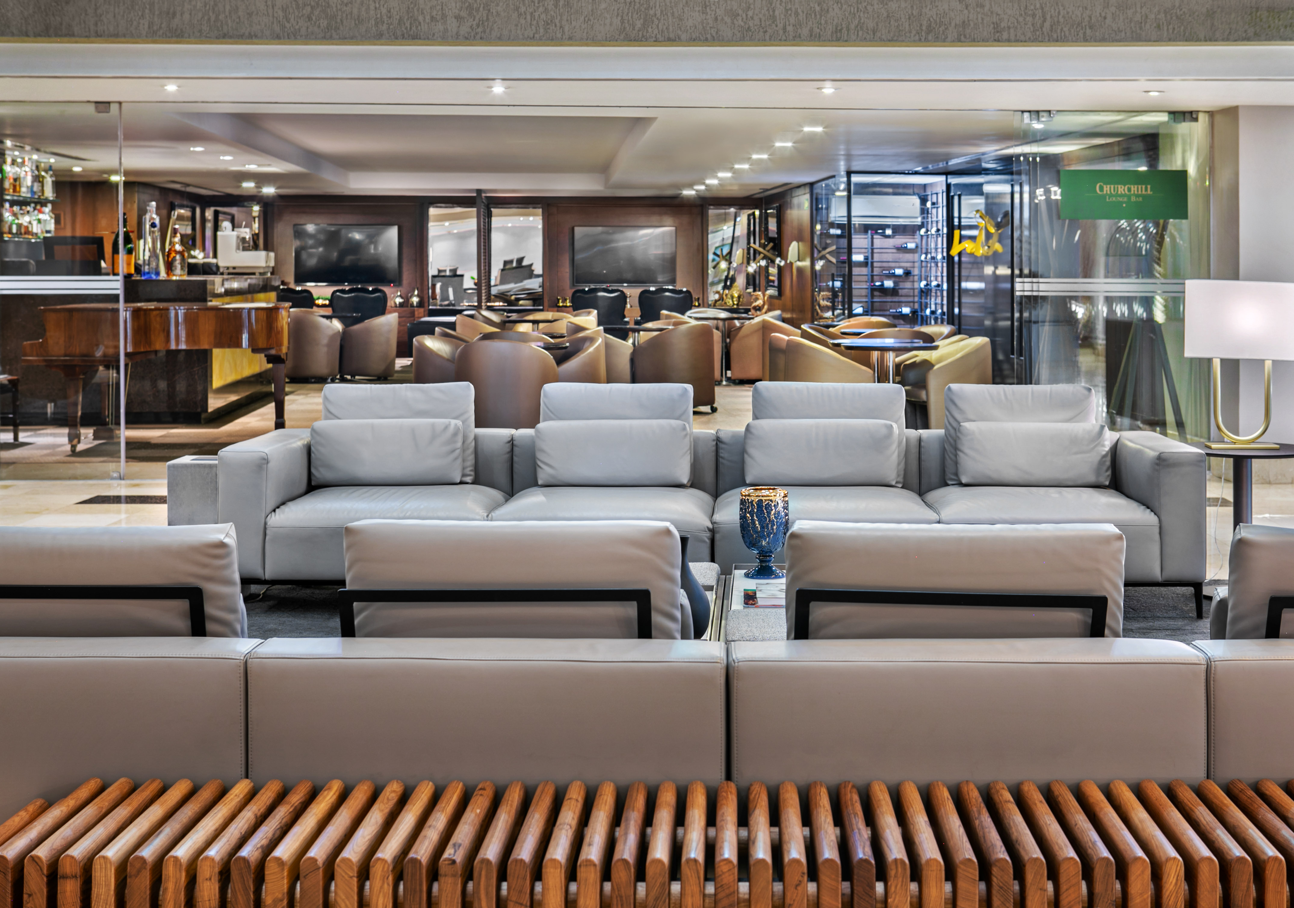 Churchill Lounge Bar interior with grey sofas, grand piano, and wine cellar.