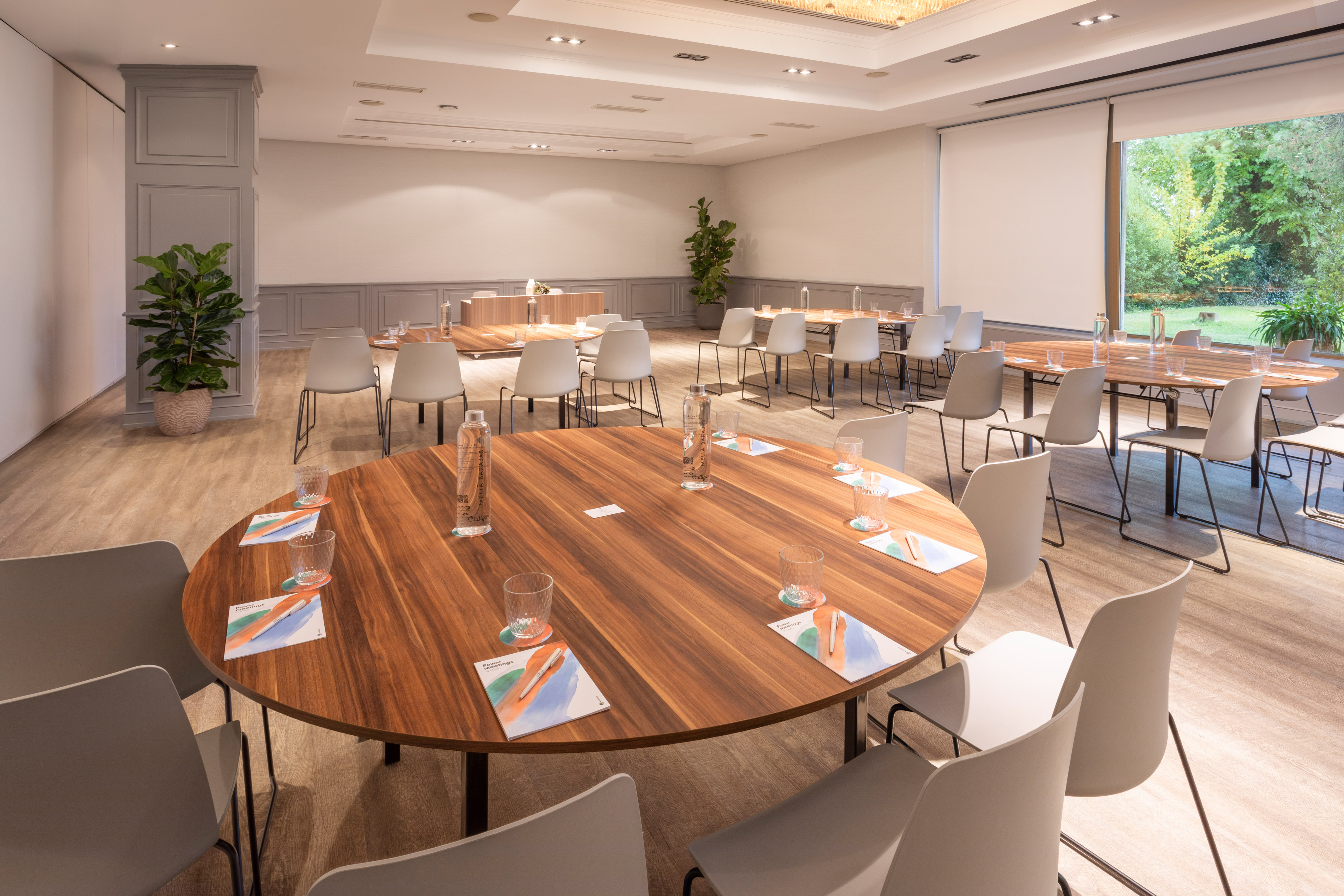Modern meeting room with wooden tables, grey chairs, and a garden view.
