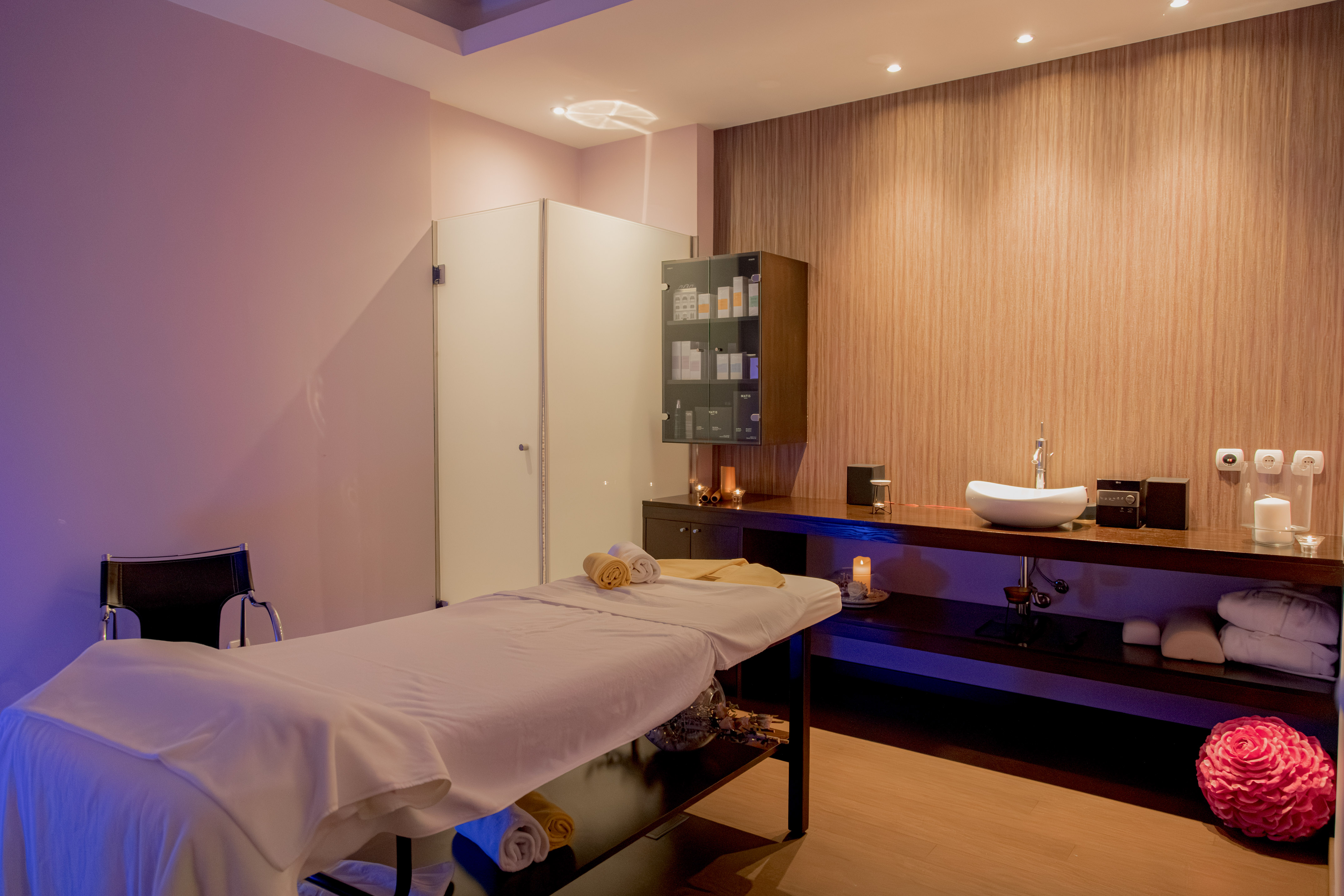 Wellness spa room with massage table, white sink, and soft ambient lighting.