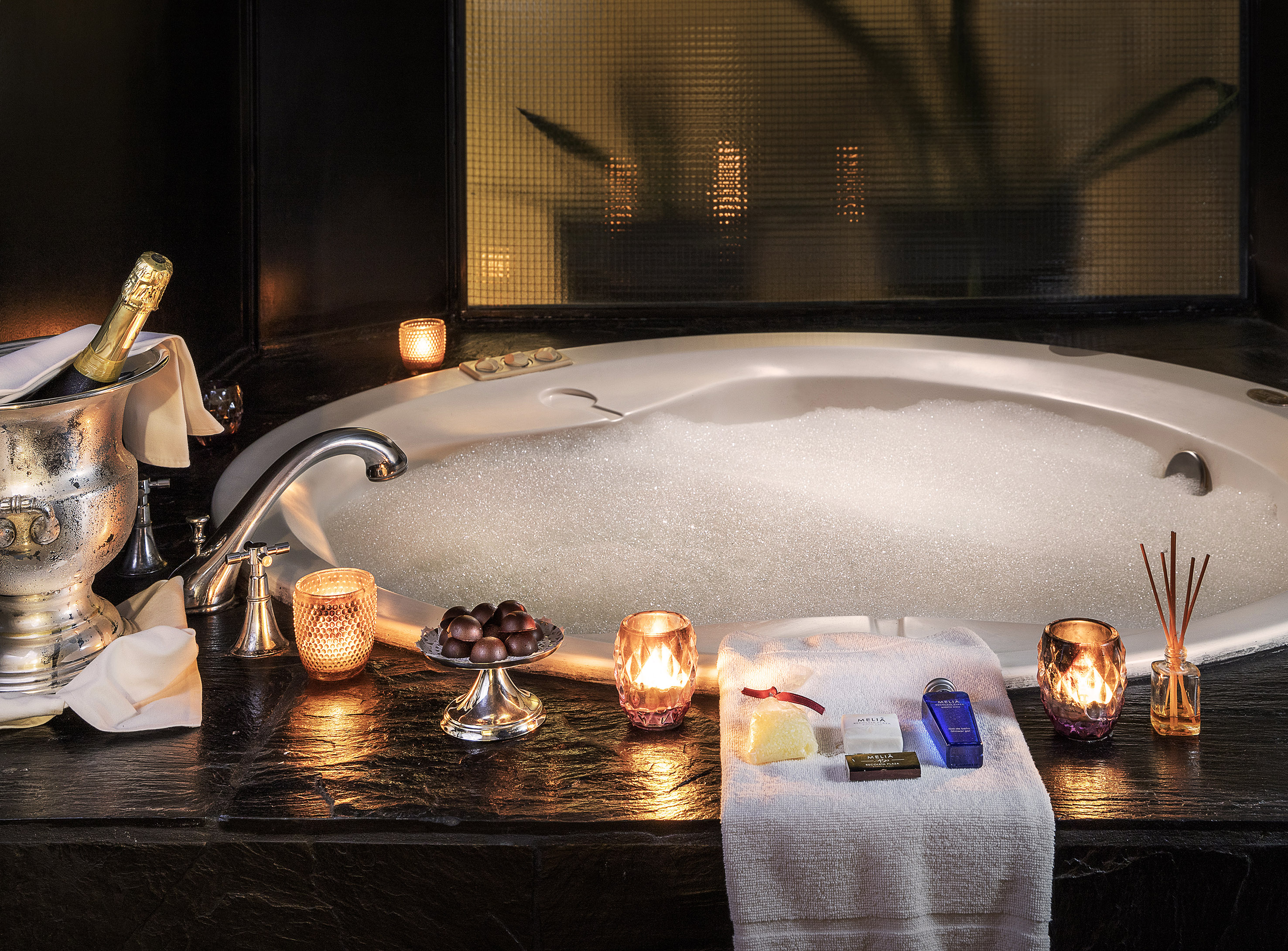 Romantic bubble bath with champagne, chocolates, and warm candles.