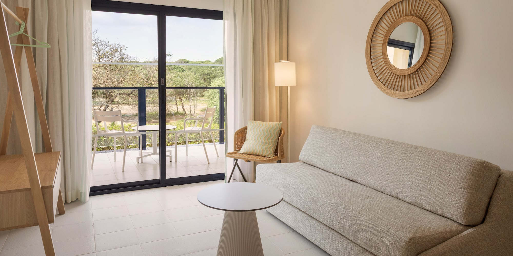 Modern hotel suite living area with balcony, sofa, and natural outdoor view.
