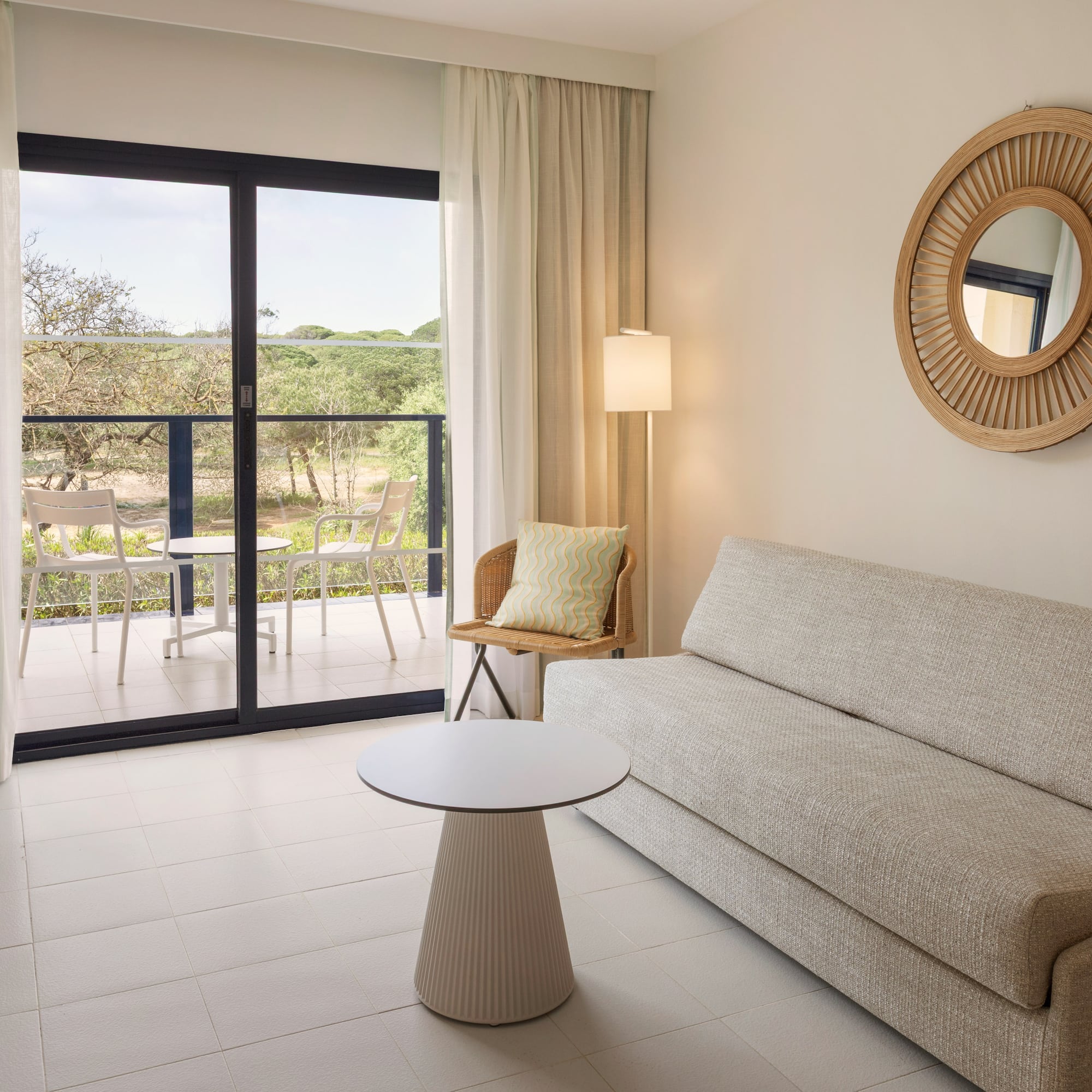 Modern hotel suite living area with balcony, sofa, and natural outdoor view.