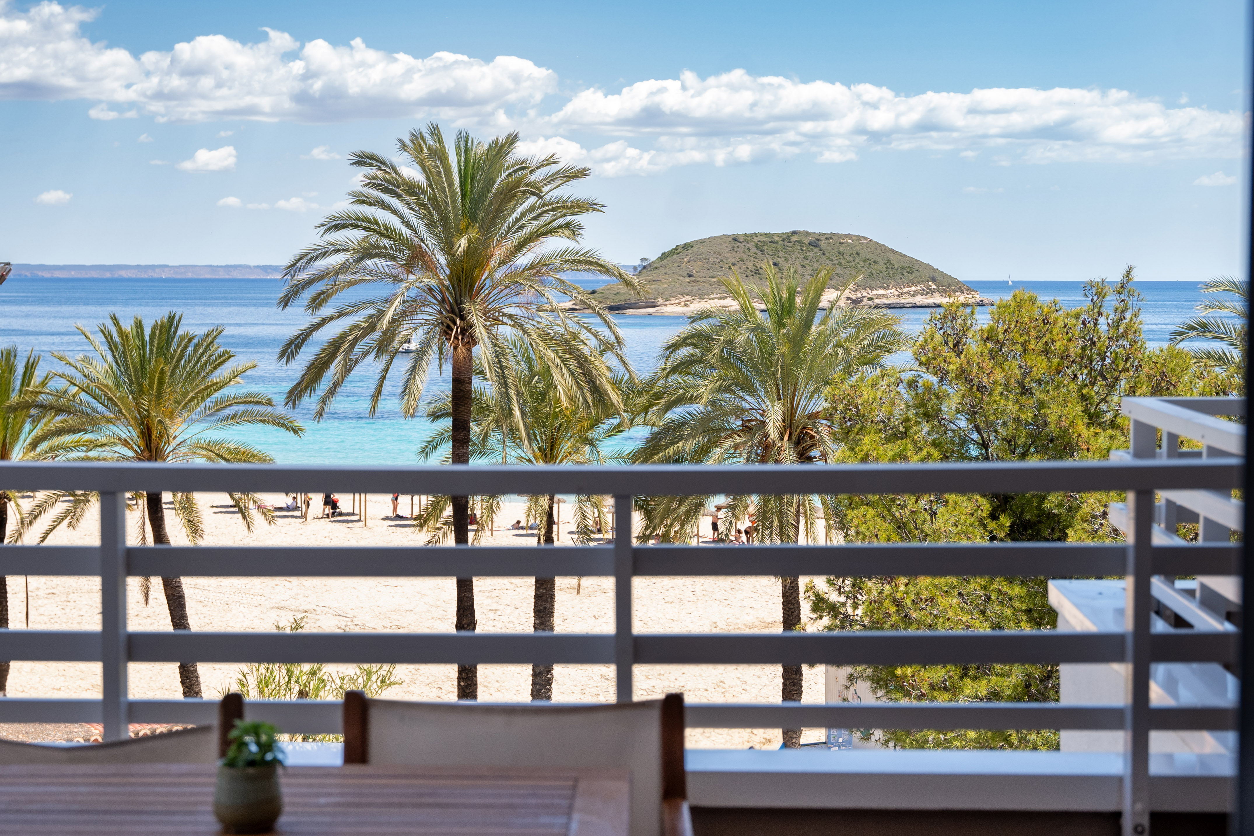 Balcony view of a tropical beach, palm trees, turquoise ocean, and distant island.