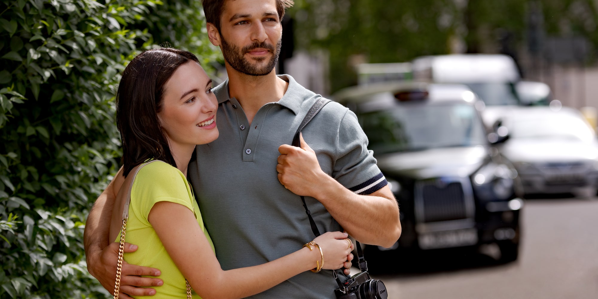 Couple embracing in London street, man with camera, black taxi in background.