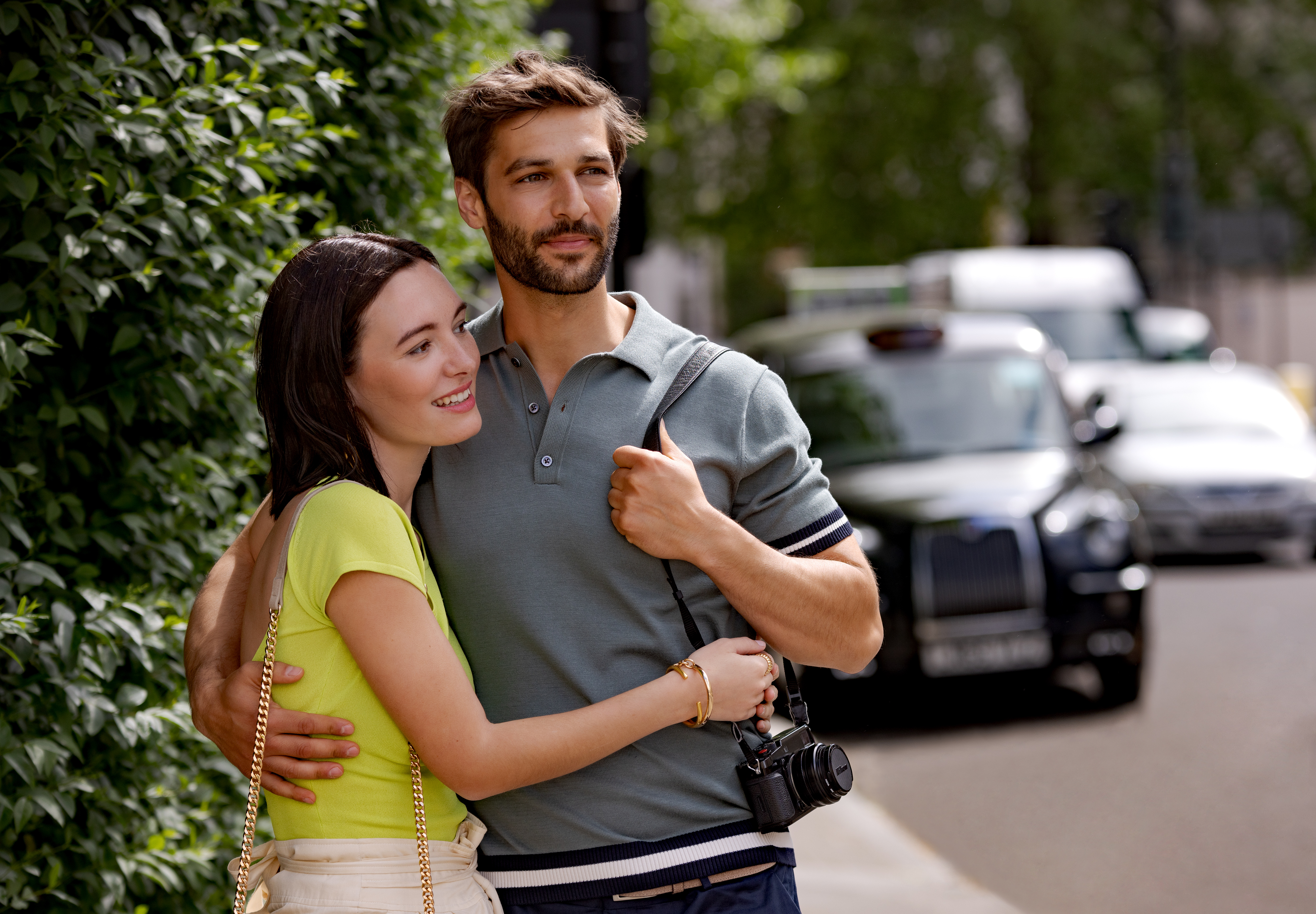 Couple embracing in London street, man with camera, black taxi in background.