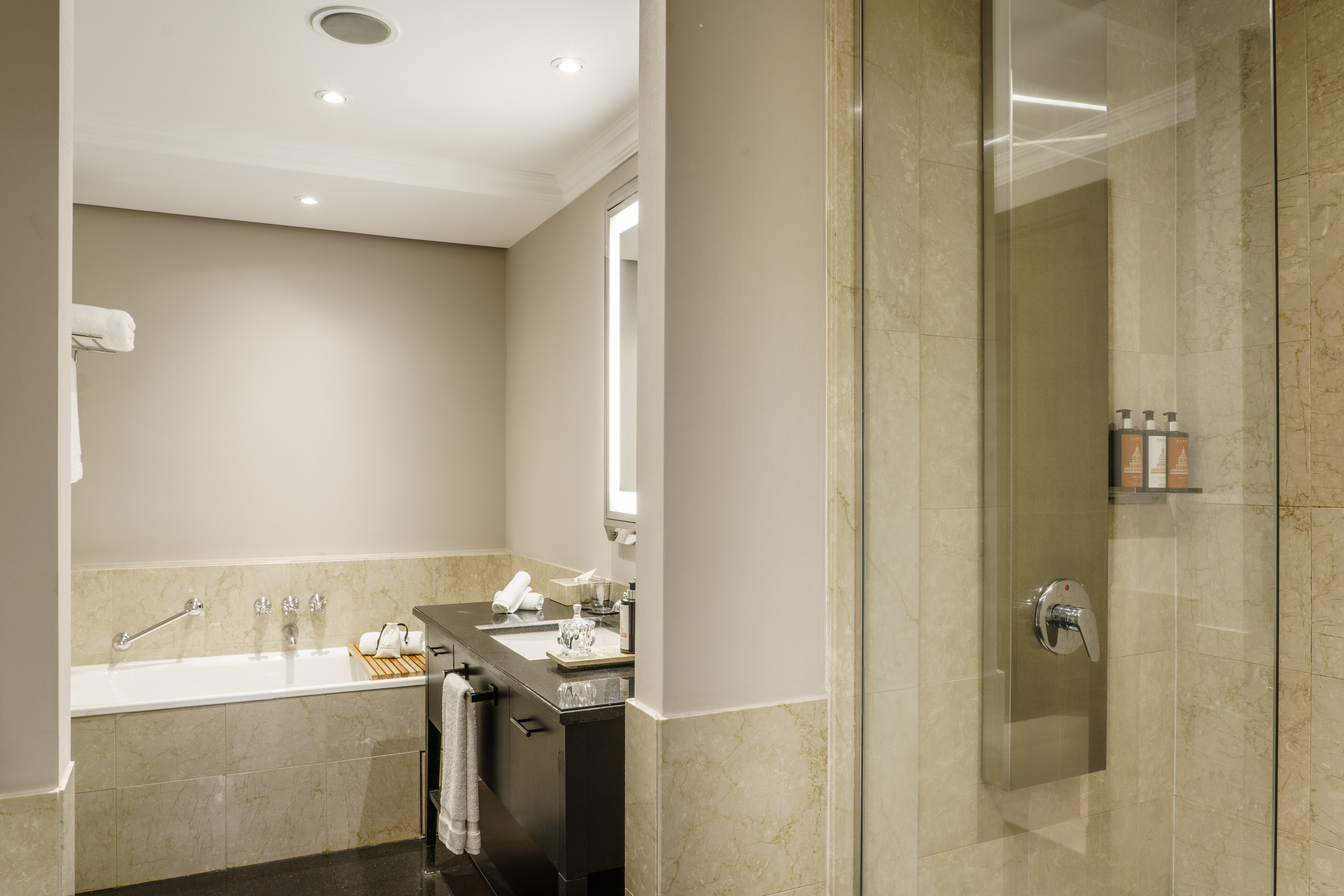 Hotel bathroom with deep tub, modern vanity, and glass shower enclosure.