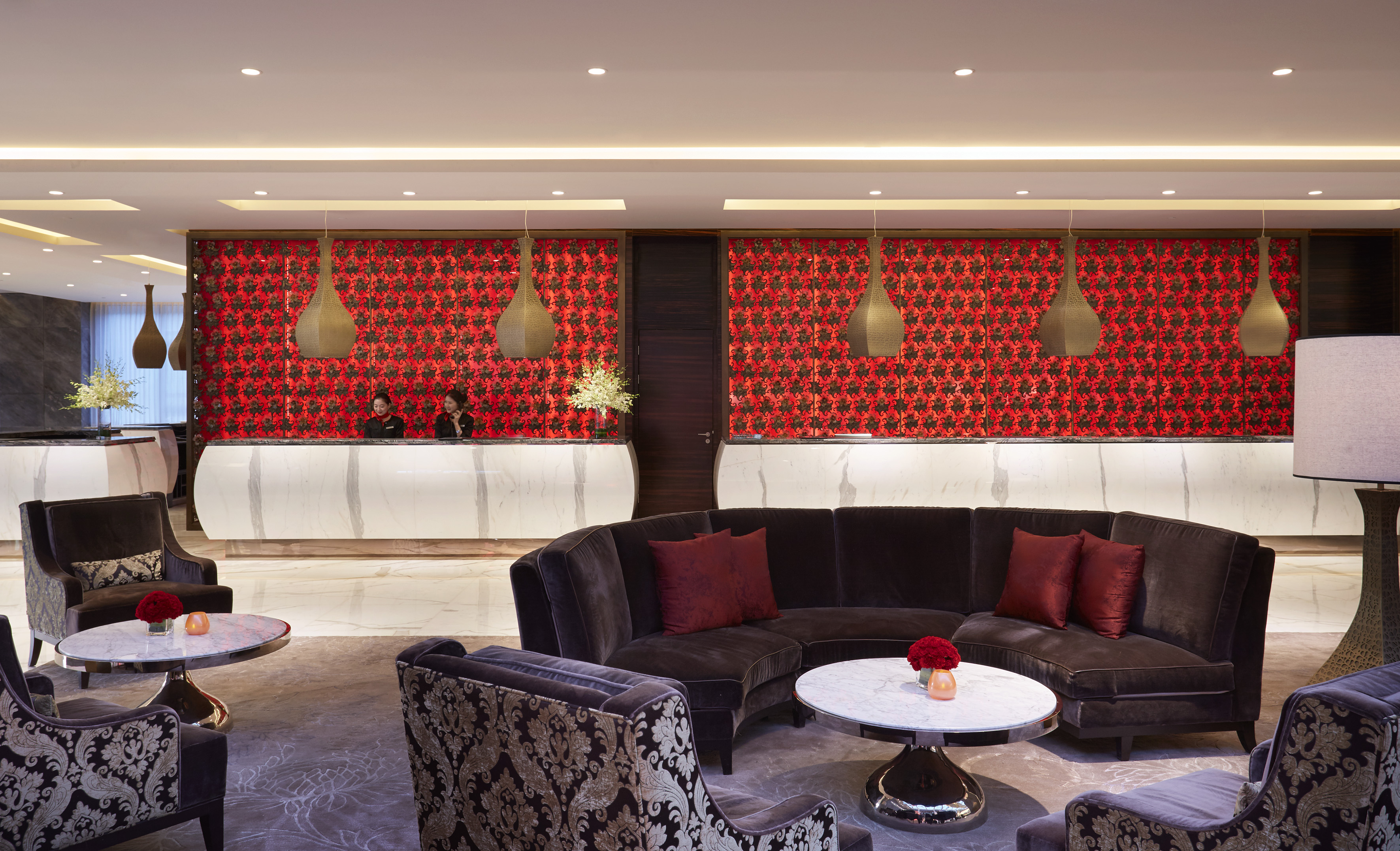 Luxury hotel lobby with reception desk, red patterned wall, and lounge seating.