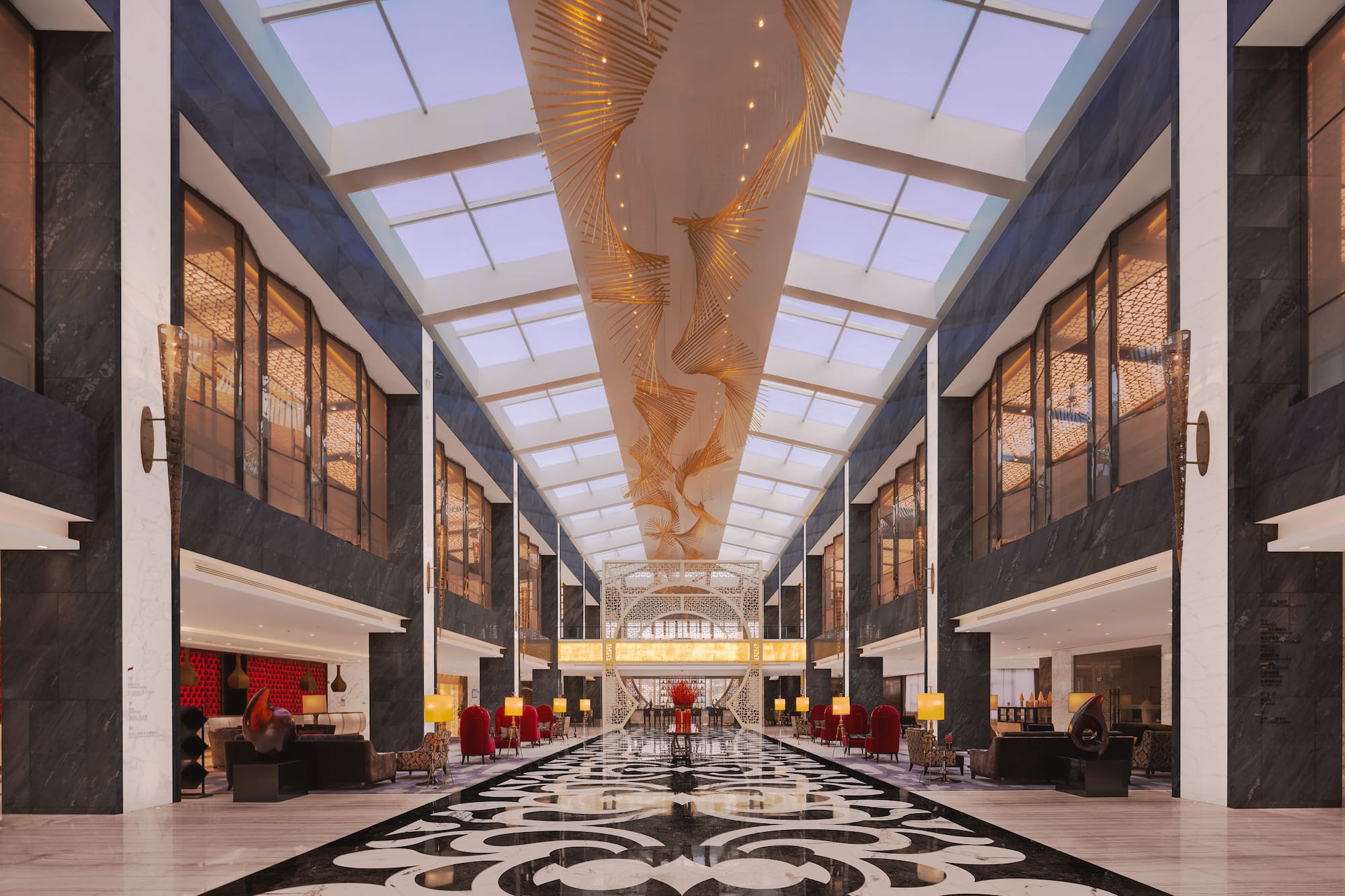 Luxury hotel lobby, ornate chandelier, skylights, and patterned marble floor.