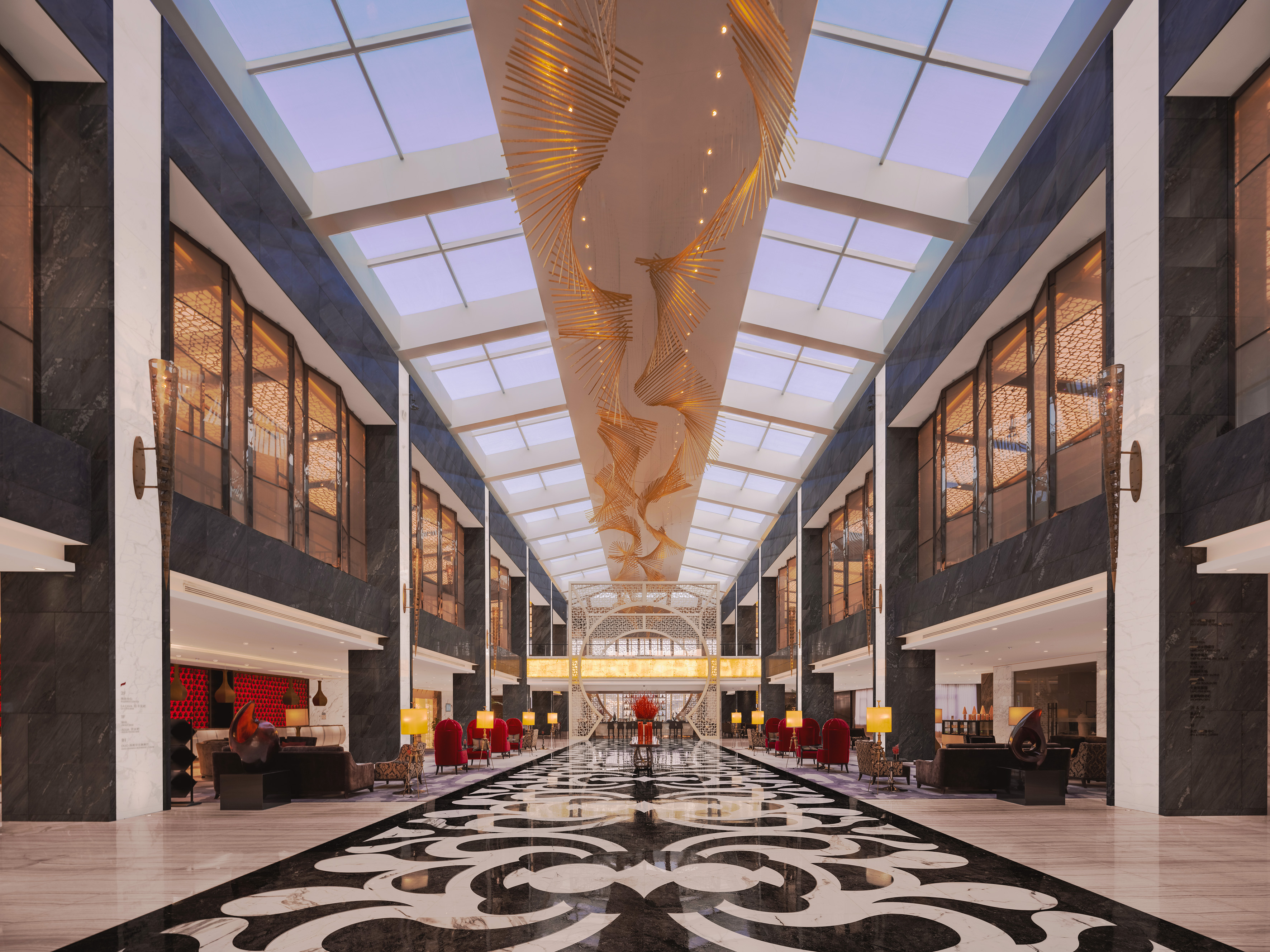 Luxury hotel lobby, ornate chandelier, skylights, and patterned marble floor.