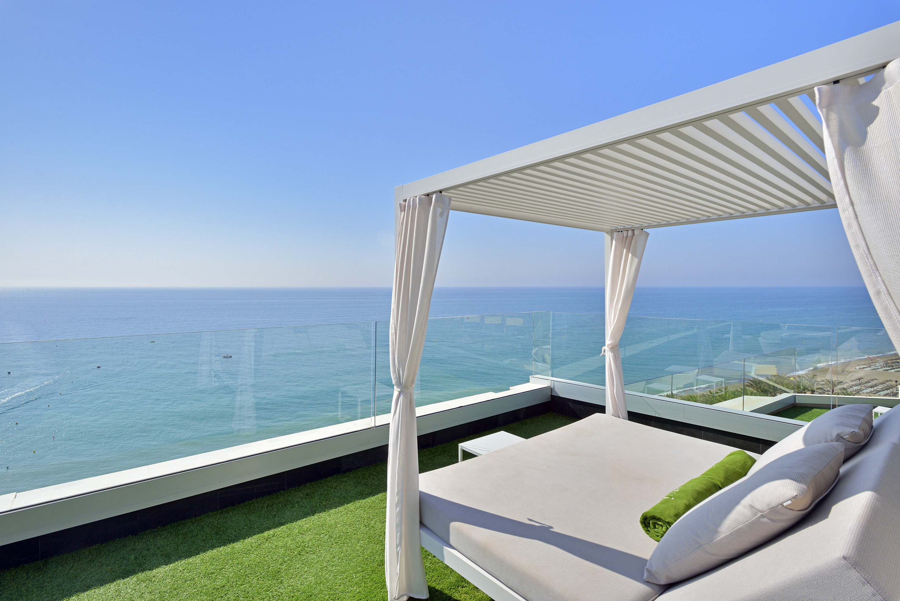 Luxury rooftop daybed with ocean view, white pergola, and artificial grass.