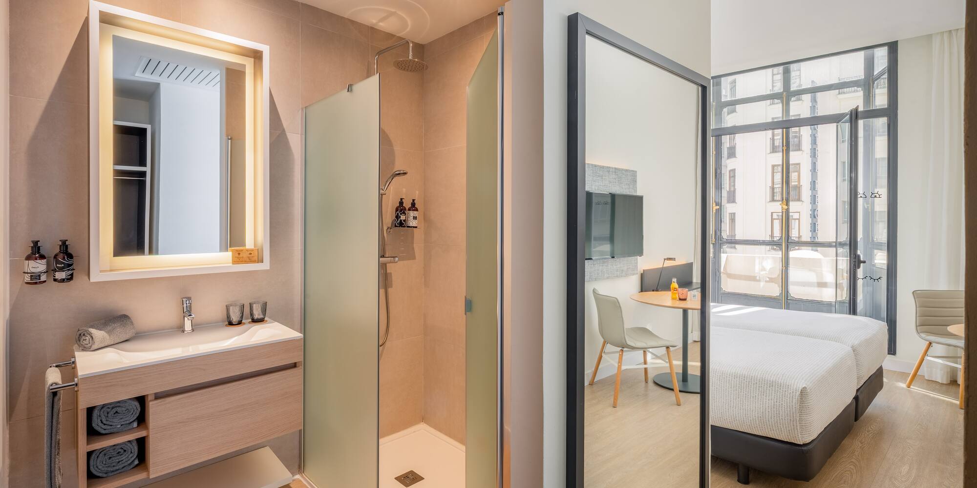 Modern hotel bathroom with walk-in shower, vanity, and twin beds reflected.