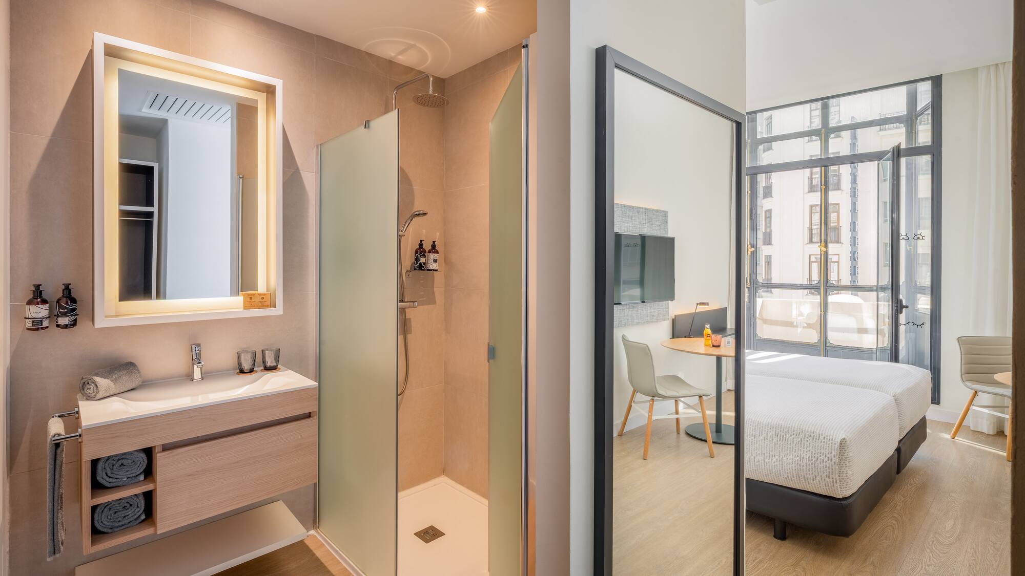 Modern hotel bathroom with walk-in shower, vanity, and twin beds reflected.