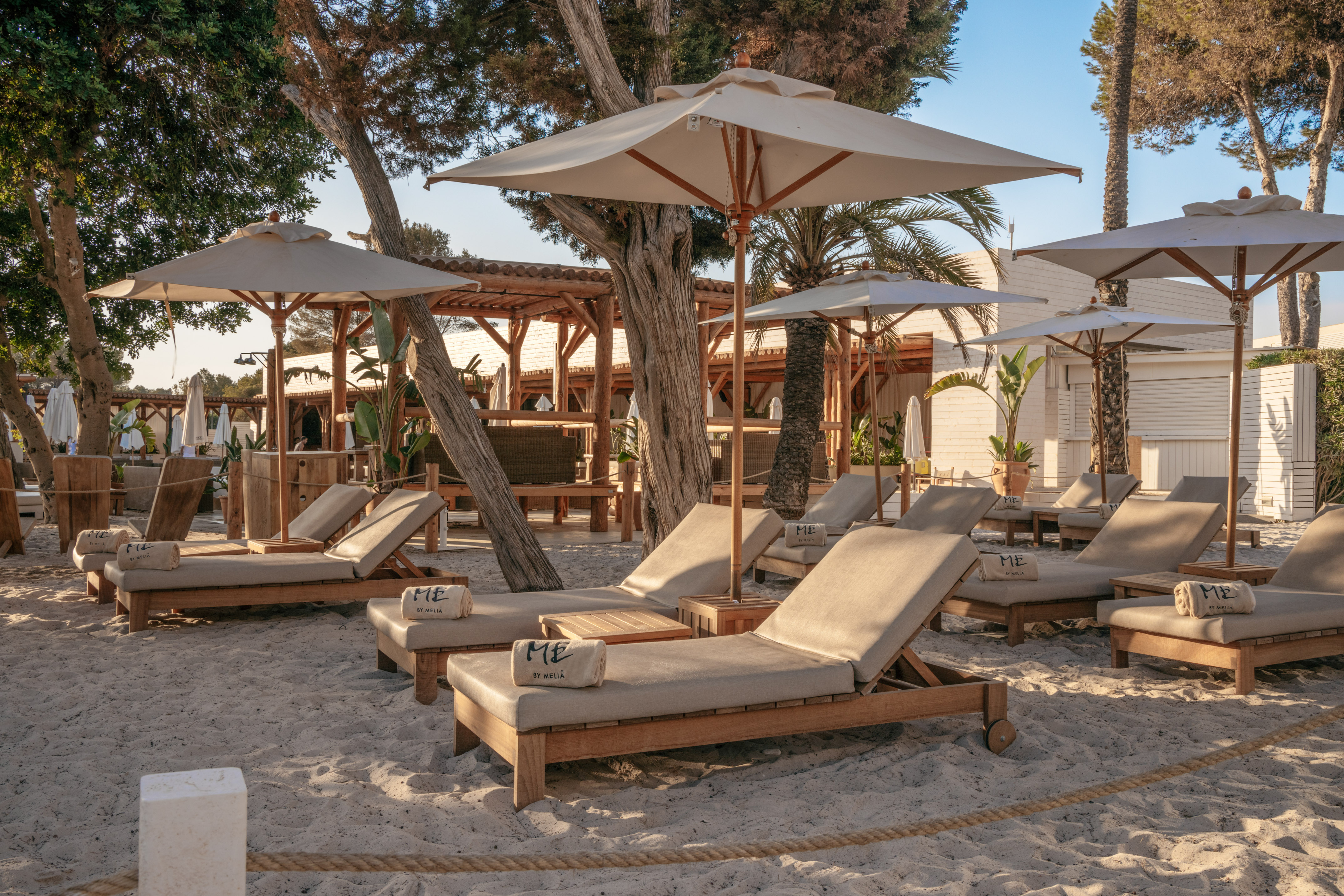 Resort beach with wooden sun loungers, umbrellas, and ME by Melia towels.