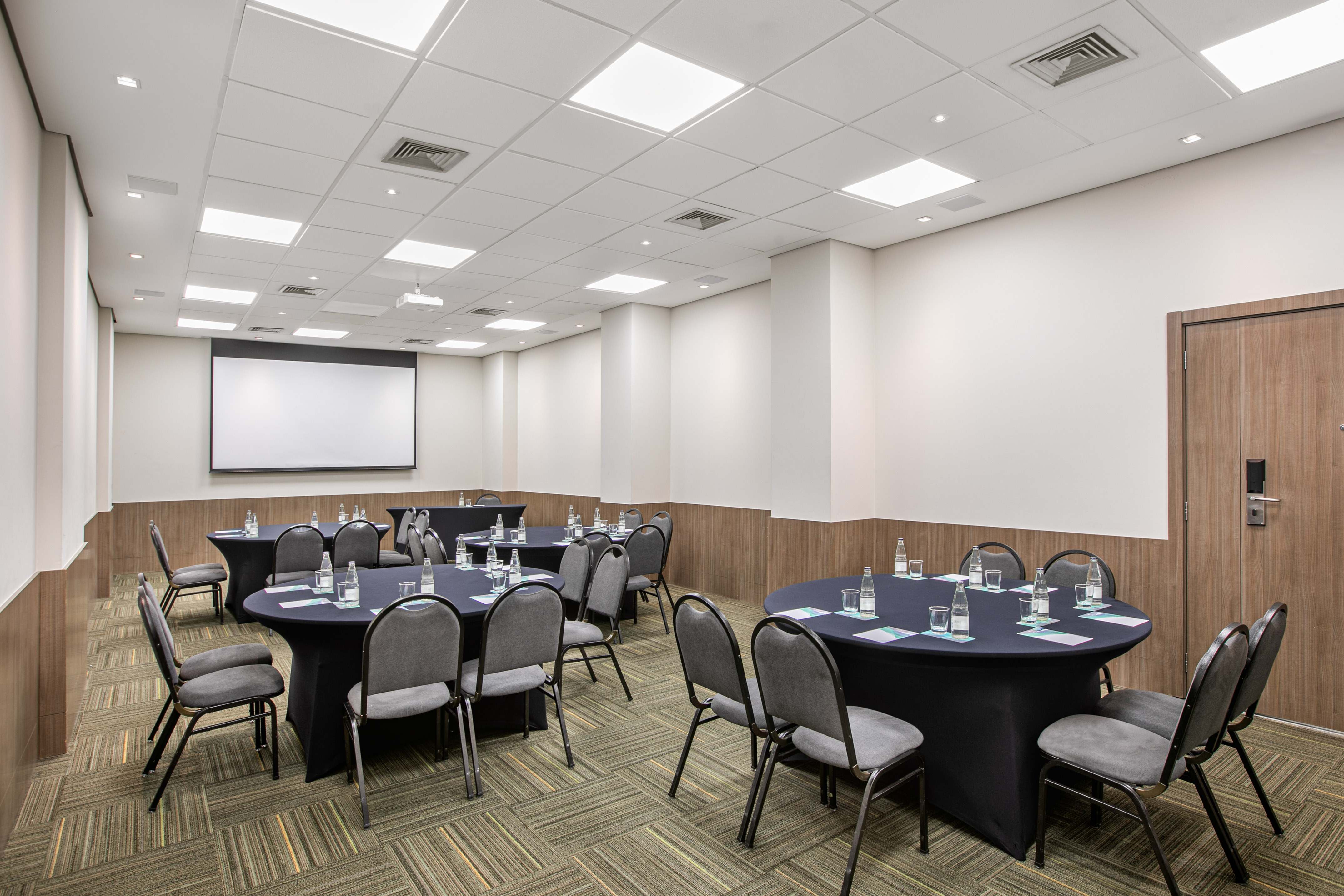 Conference room with black round tables, gray chairs, and projector screen.