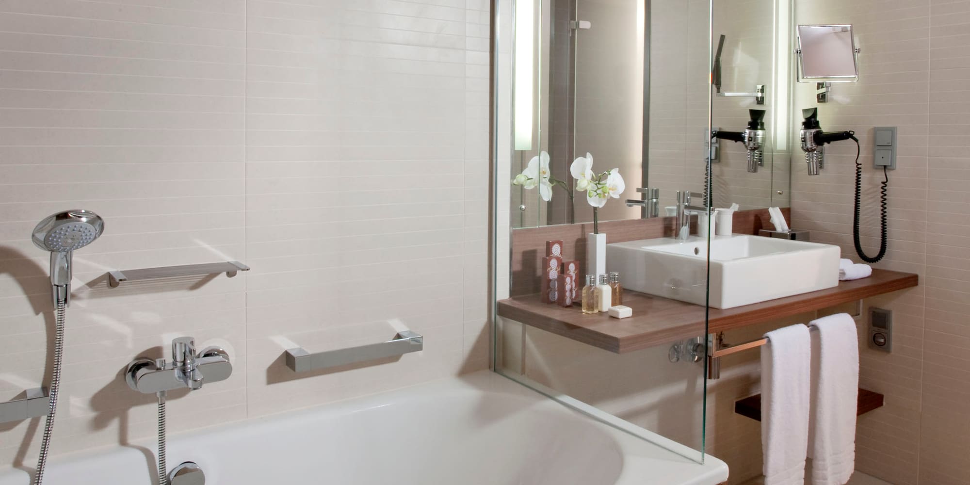 Modern bathroom with white bathtub, wooden vanity, sink, and glass partition.
