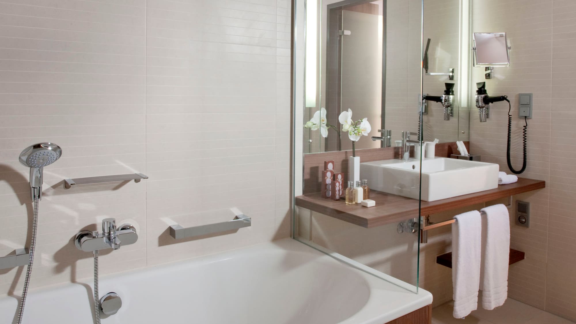 Modern bathroom with white bathtub, wooden vanity, sink, and glass partition.