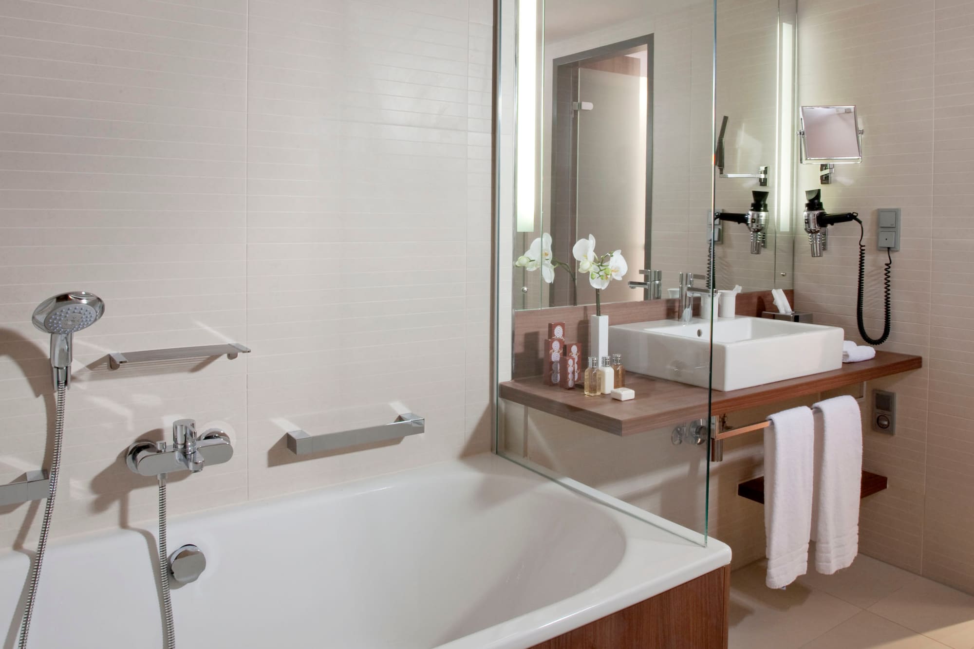 Modern bathroom with white bathtub, wooden vanity, sink, and glass partition.