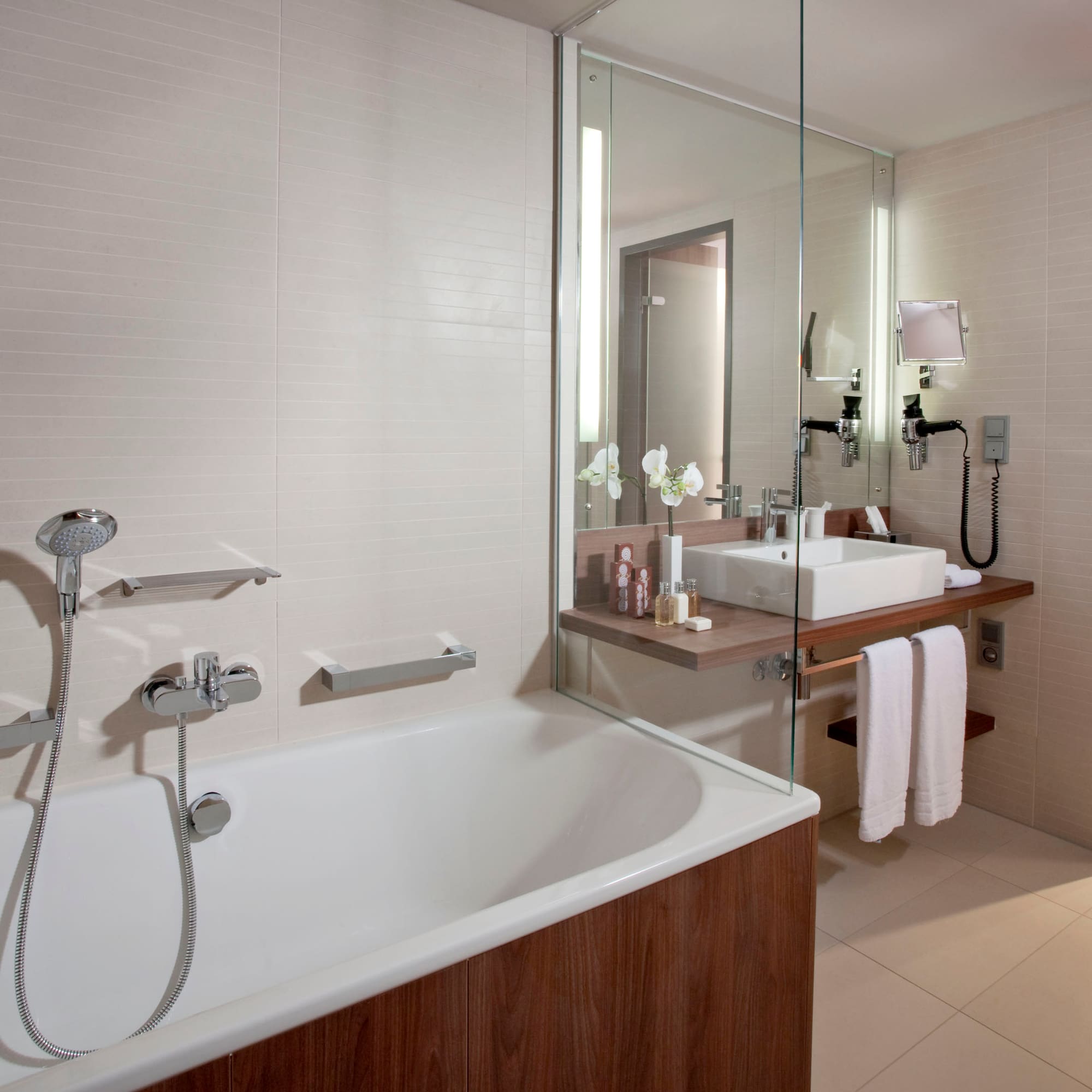 Modern bathroom with white bathtub, wooden vanity, sink, and glass partition.