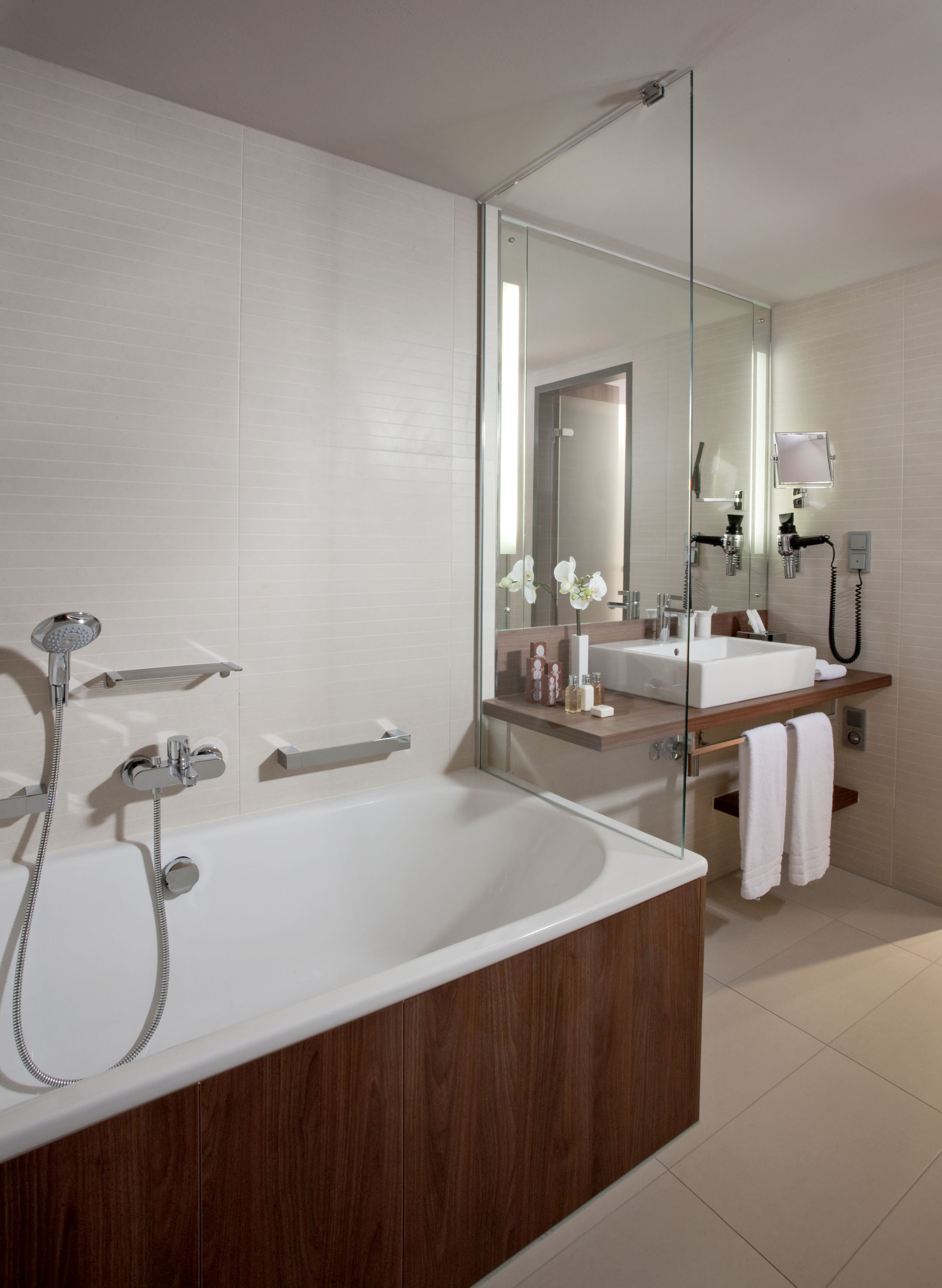 Modern bathroom with white bathtub, wooden vanity, sink, and glass partition.
