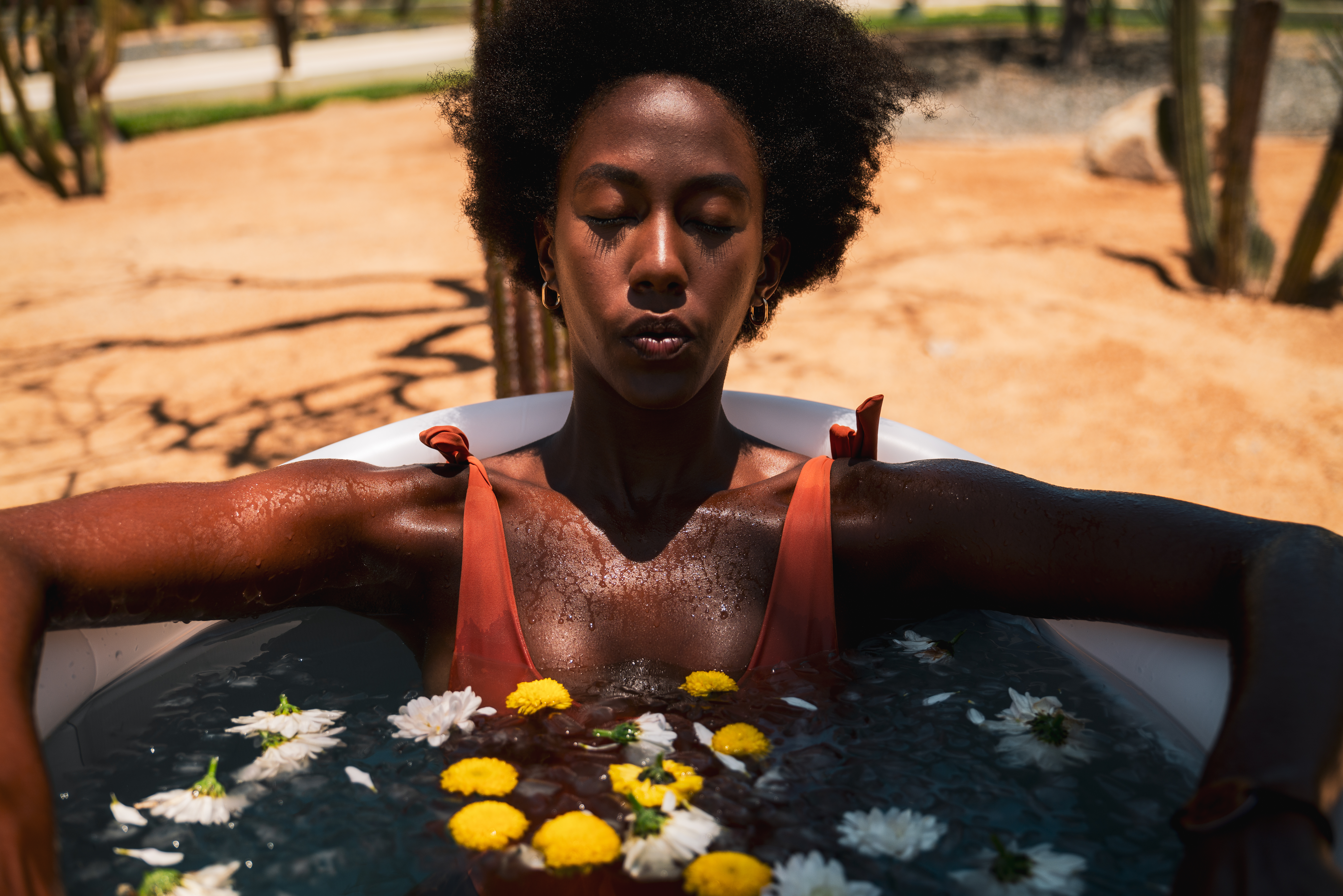 Meditating woman in outdoor flower bath amidst desert landscape.