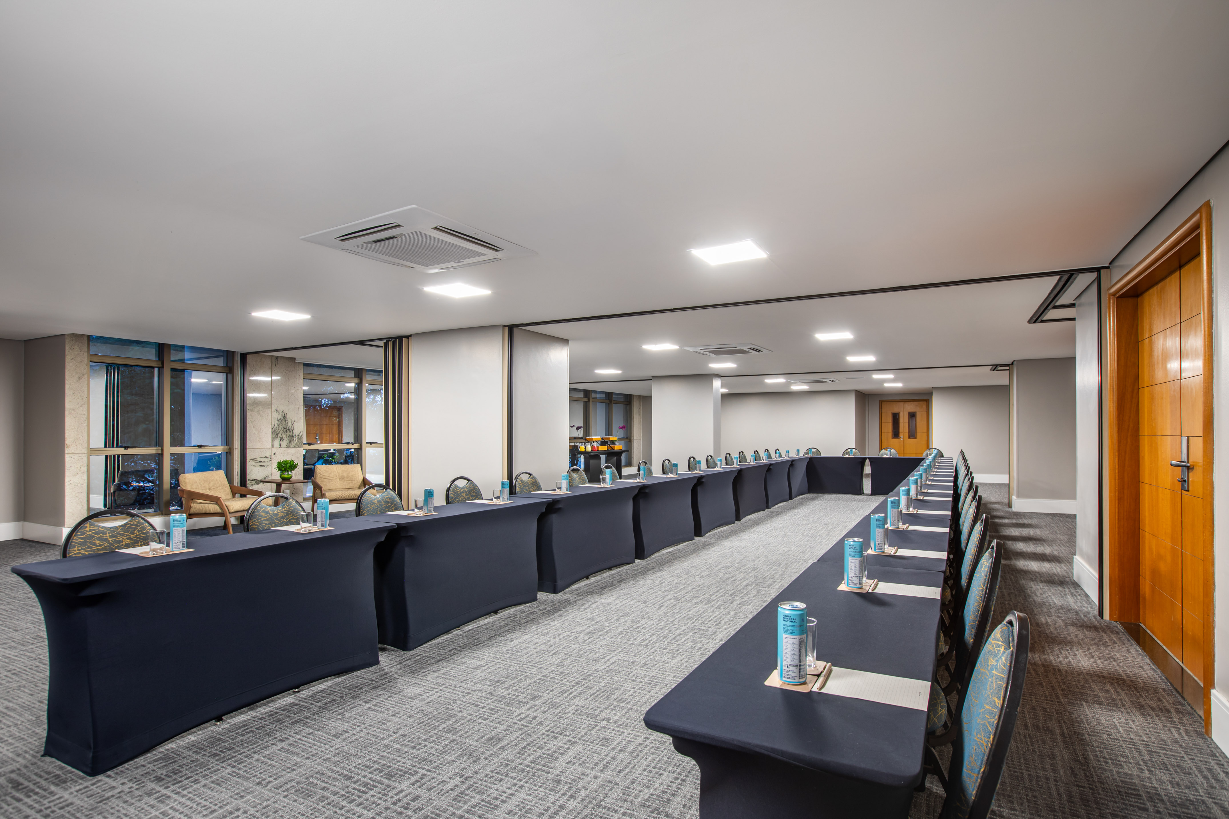 U-shaped meeting room setup with dark tables, chairs, individual drinks, and natural light.