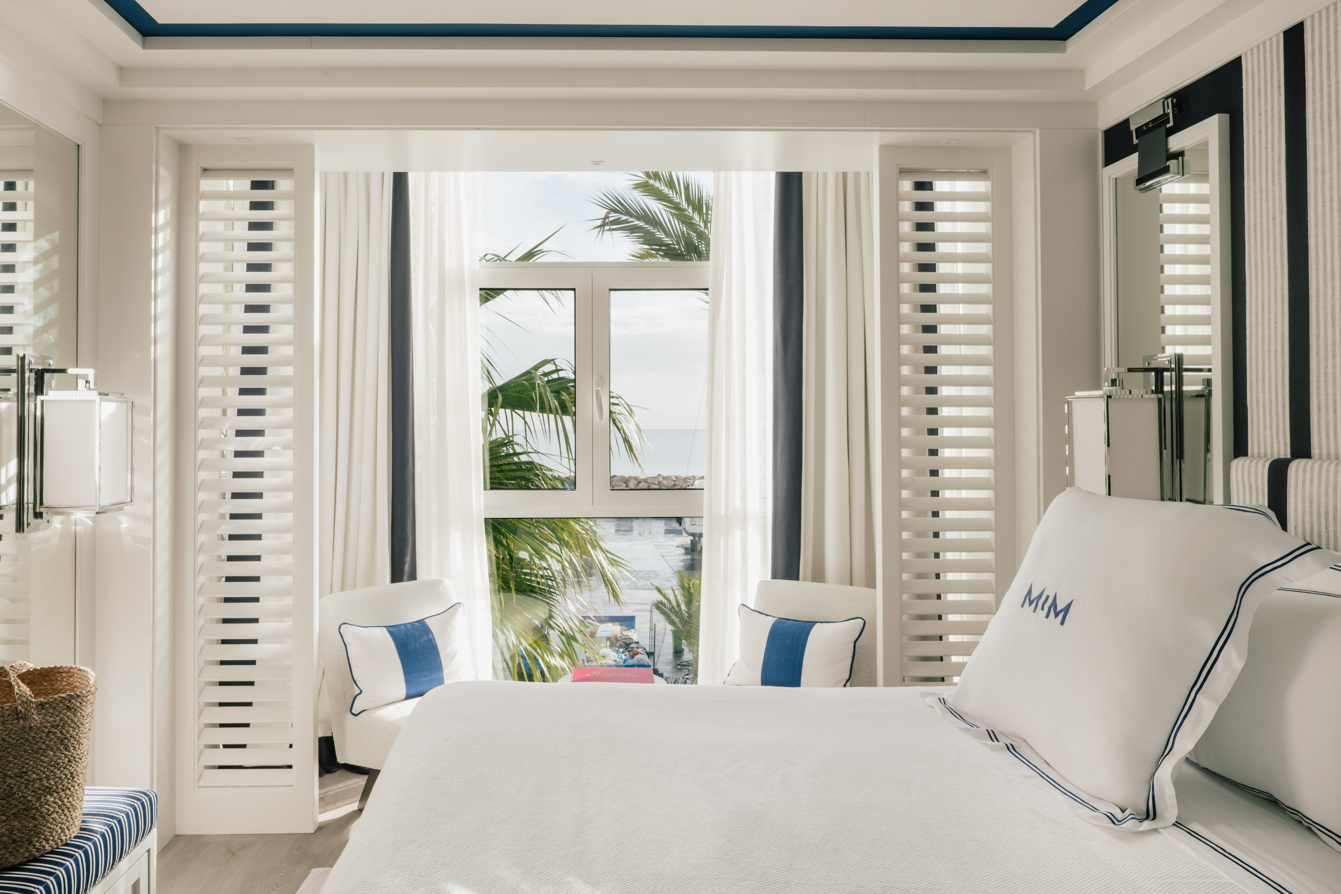 Coastal hotel bedroom with ocean view, palm trees, white and blue accents.