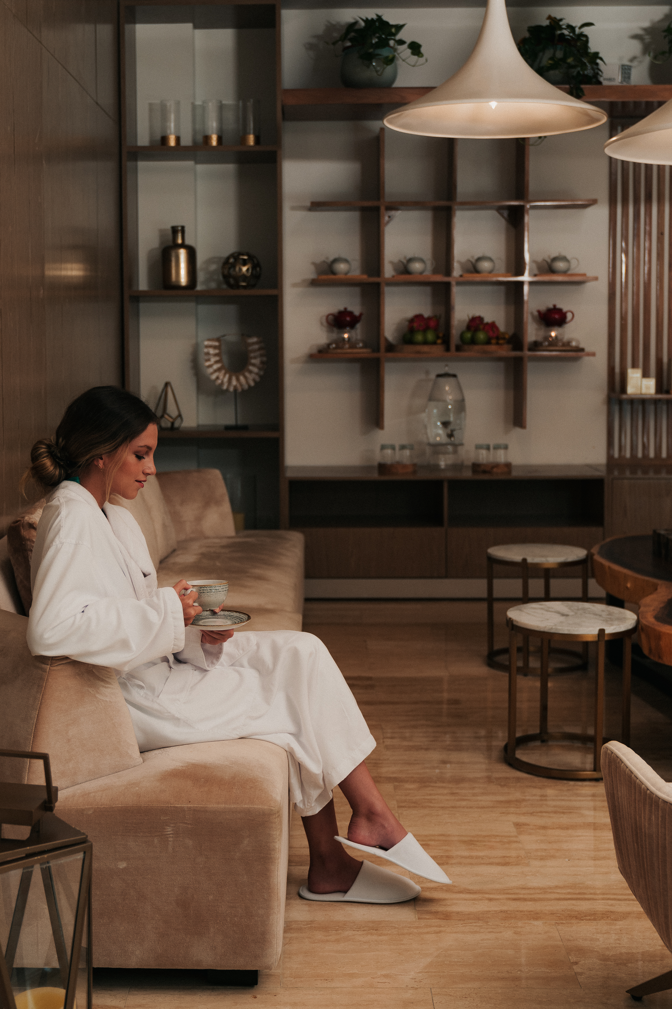 Woman relaxing in white bathrobe, sipping tea on sofa in spa lounge.