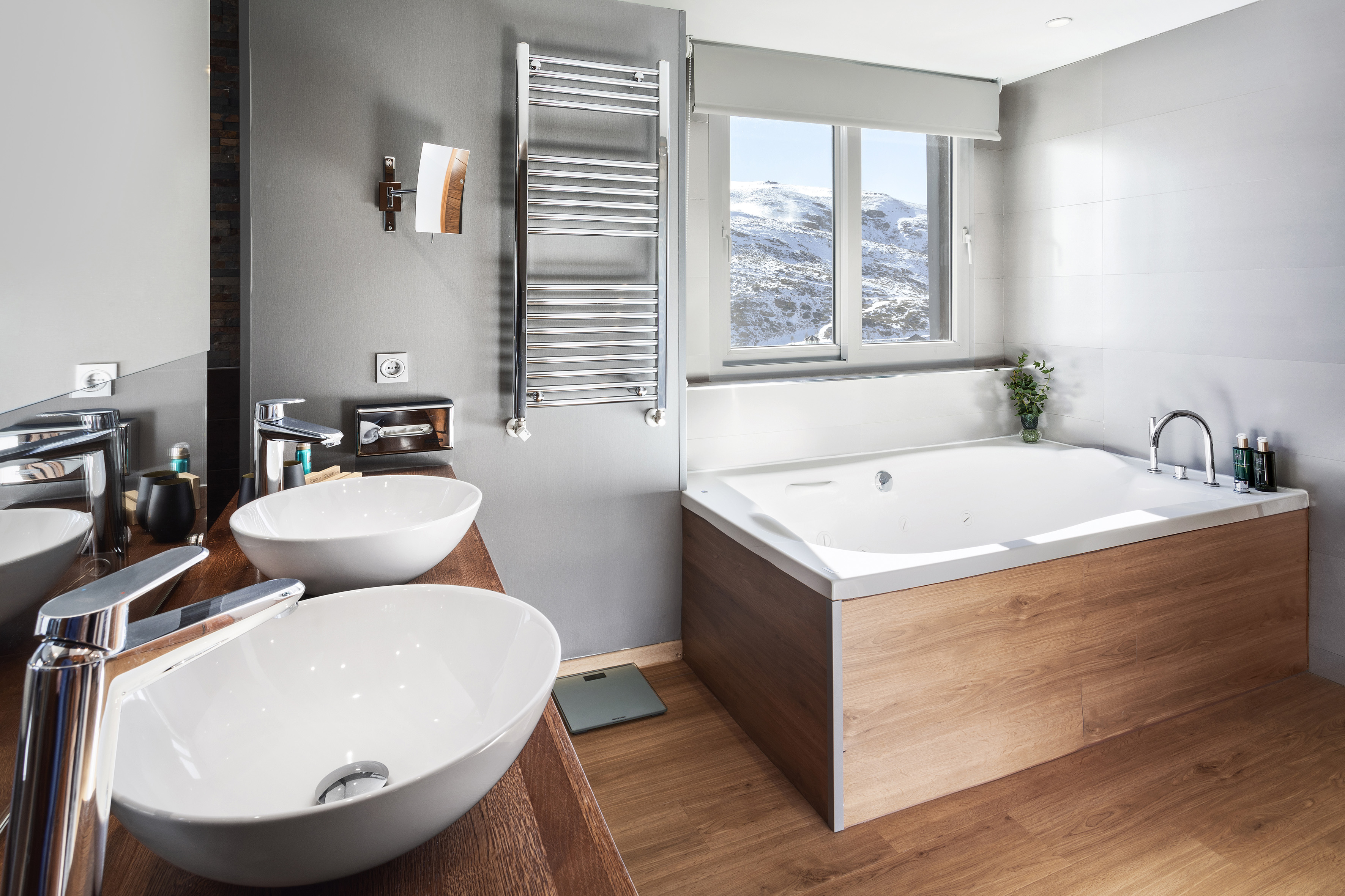 Modern bathroom with double vanity, spa tub, and snowy mountain view.